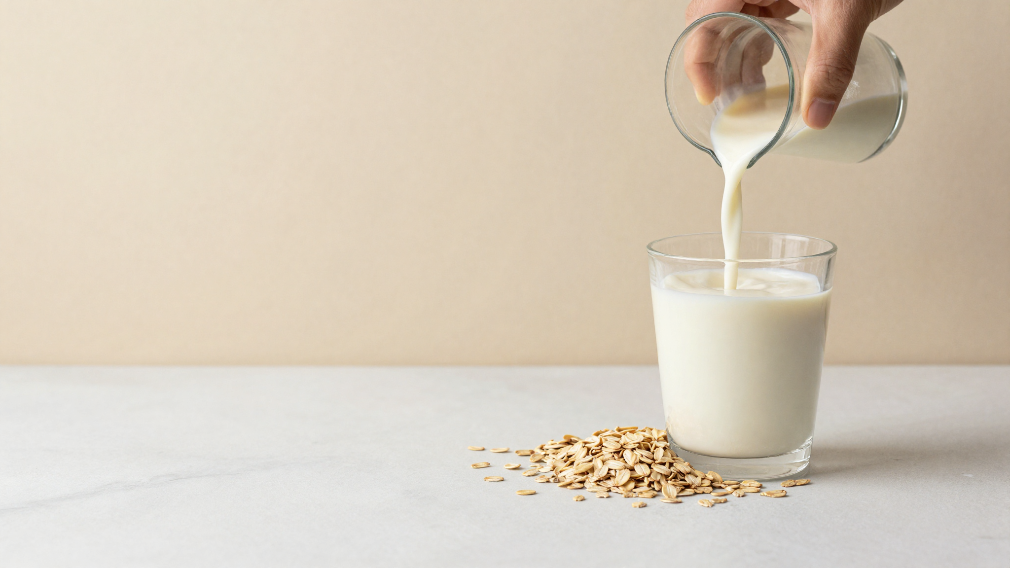 Oat milk being poured beside whole oats on a marble surface