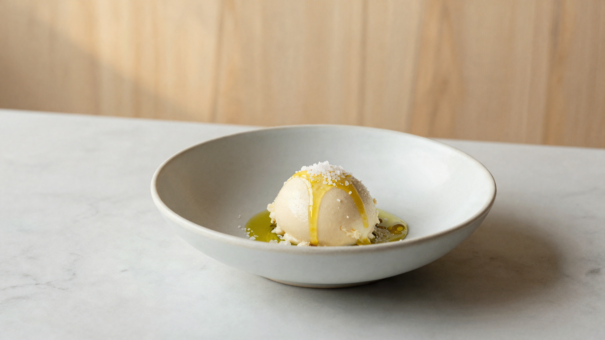 An elegant restaurant dessert of pale gelato drizzled with olive oil and sea salt flakes
