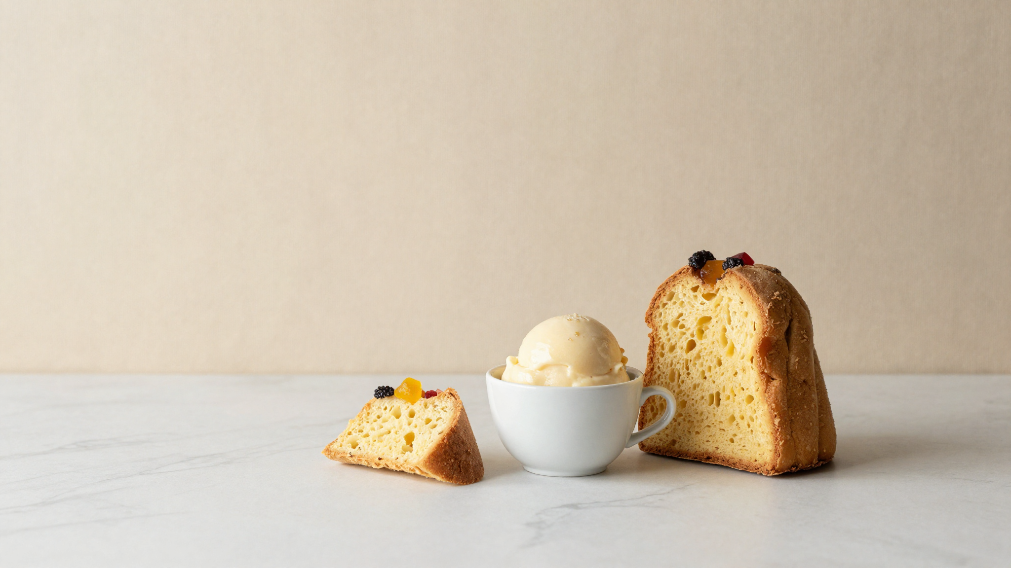 Two ceramic cups of pale festive gelato on marble beside slices of pandoro and panettone
