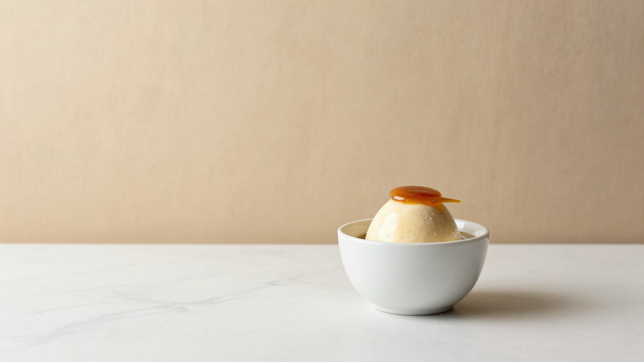 Panna cotta gelato in a small ceramic cup with vanilla bean specks on marble
