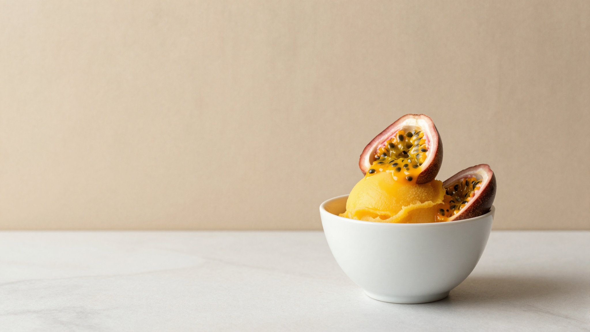 A serving of vivid orange passion fruit sorbet in a white ceramic cup garnished with fresh passion fruit halves