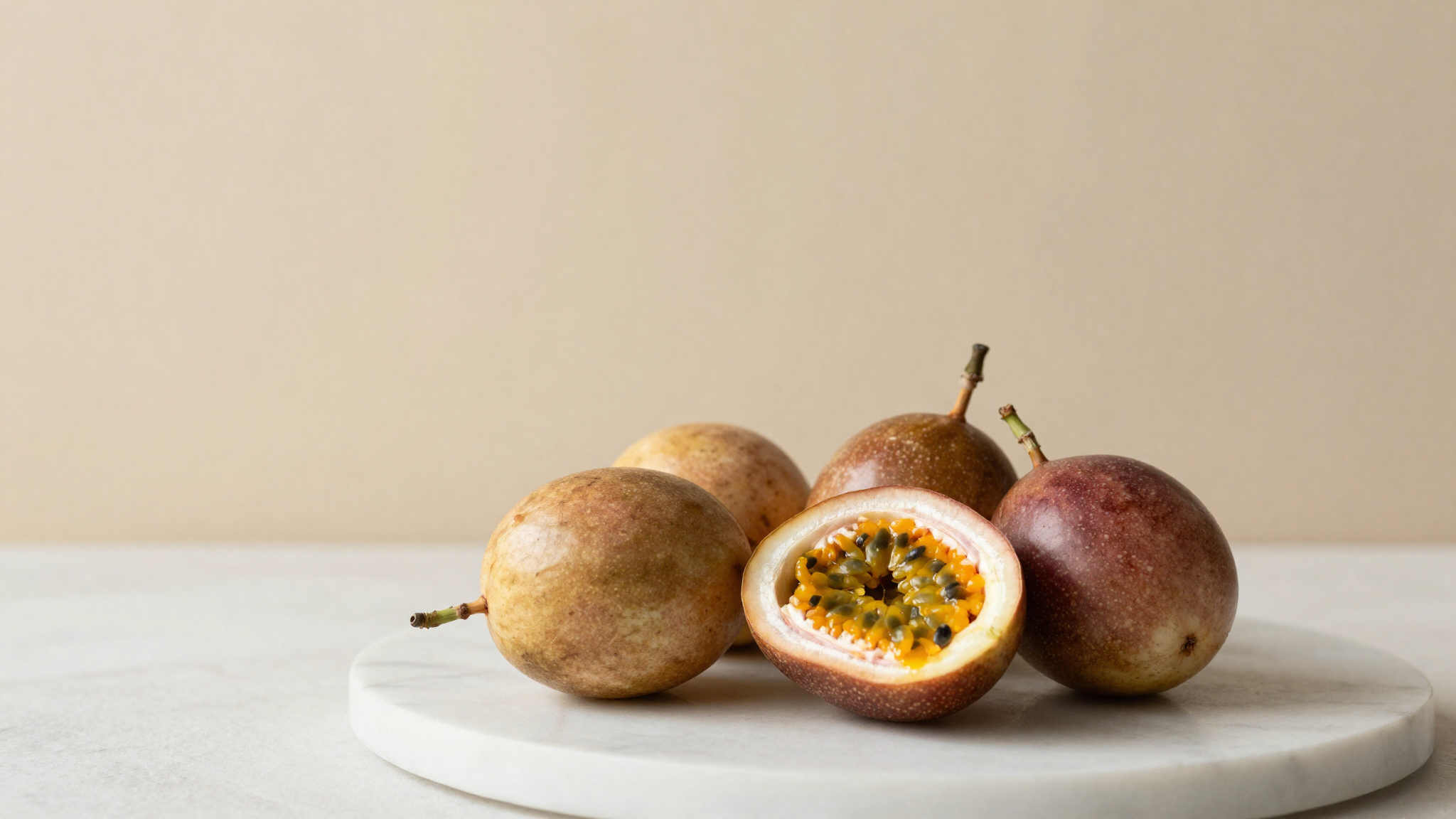 Fresh ripe passion fruit on white marble, several whole and one halved showing vivid orange pulp and seeds
