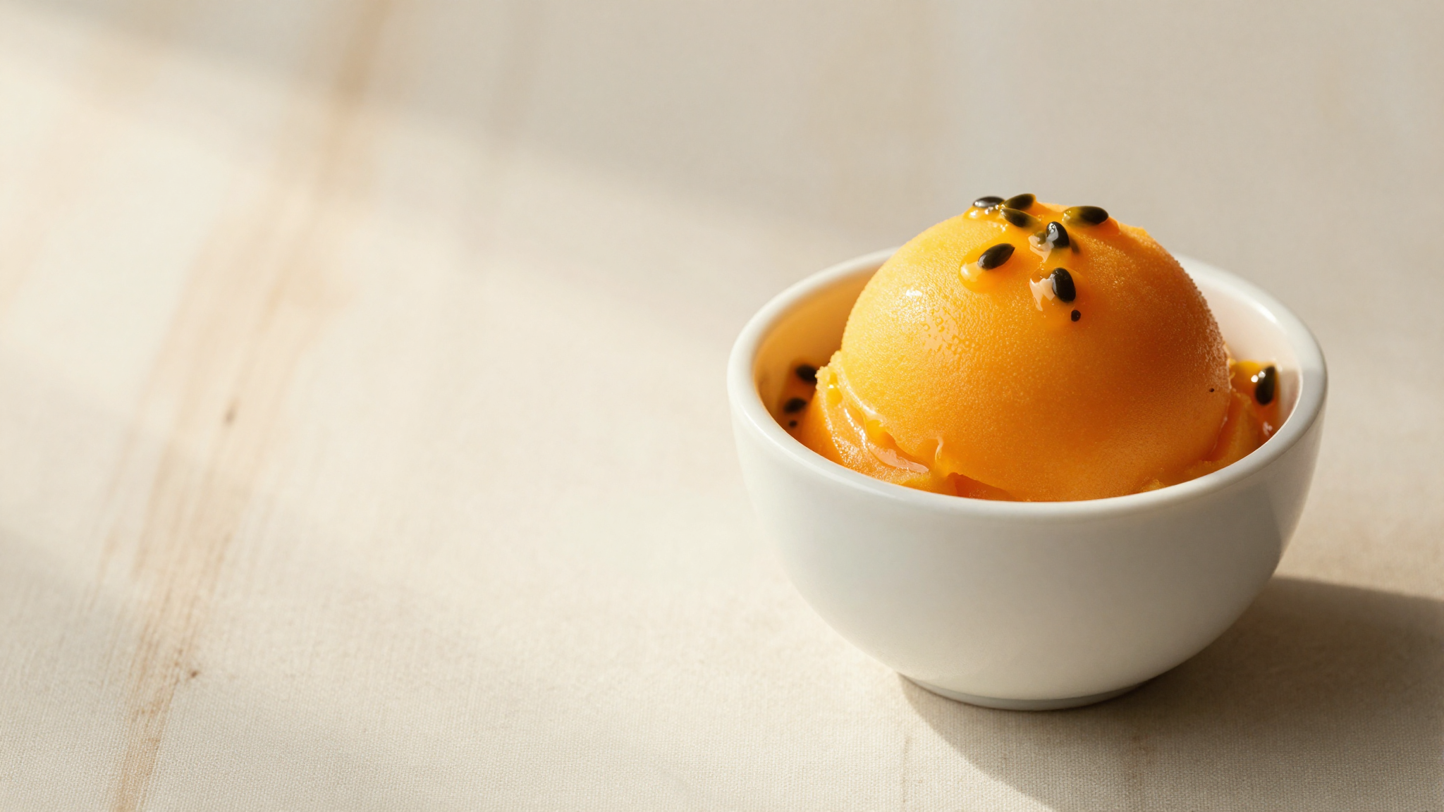 A single elegant quenelle of vivid orange passion fruit sorbet in a white ceramic cup with a few dark seeds