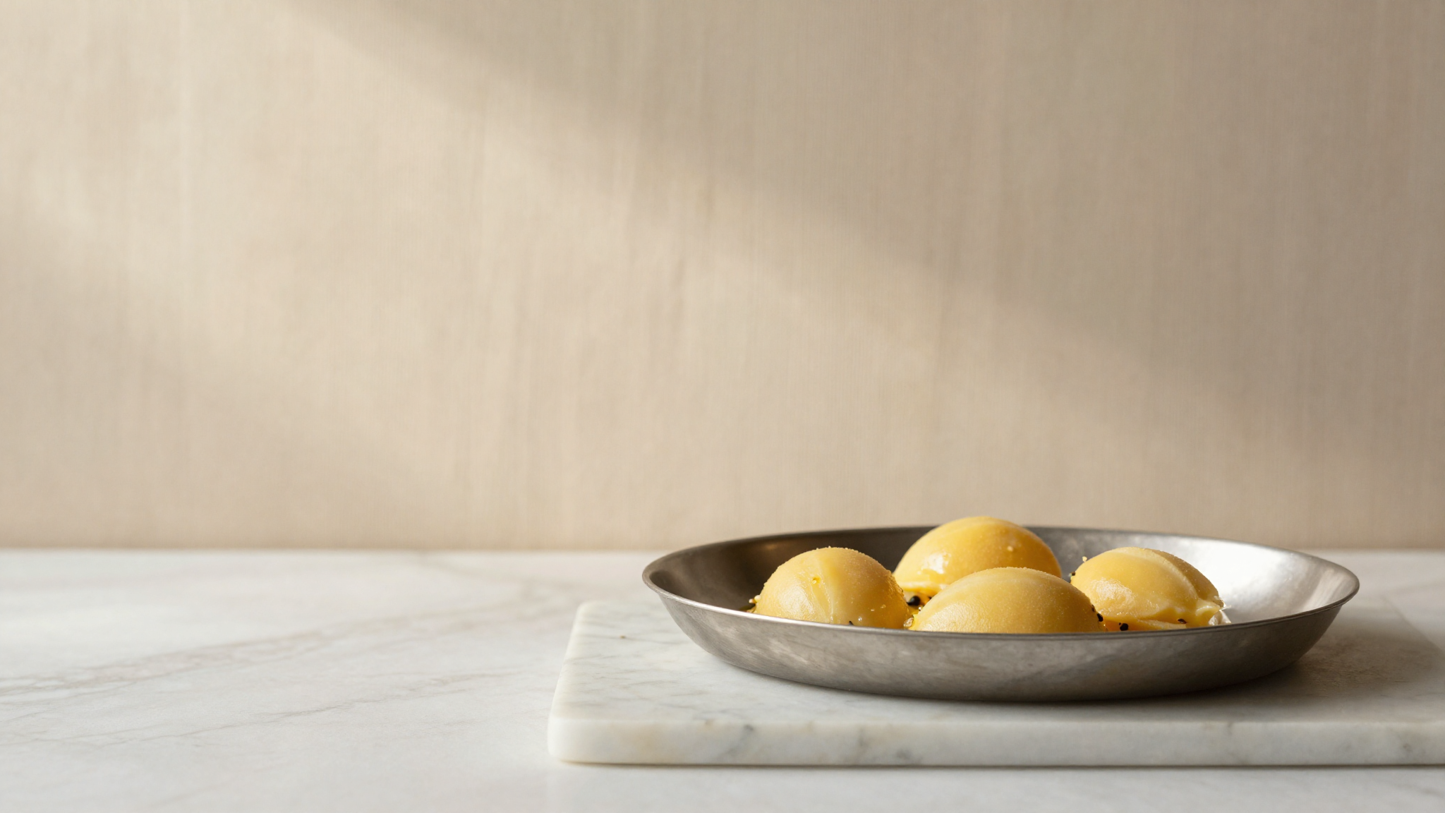 A quenelle of golden passionfruit sorbetto in a curved stainless pan