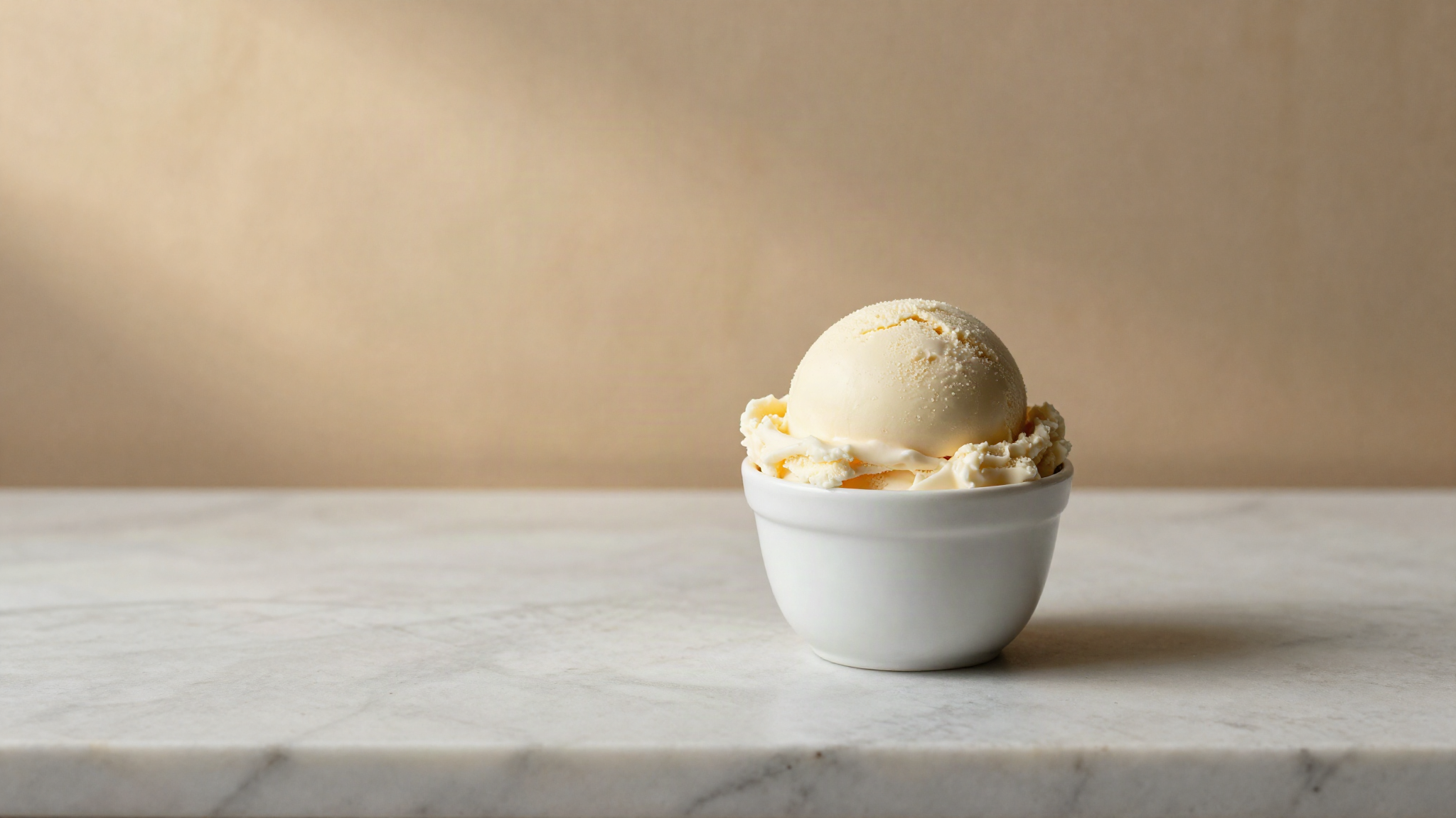 A freshly drawn scoop of pale ivory vegan gelato in a small white ceramic cup on marble