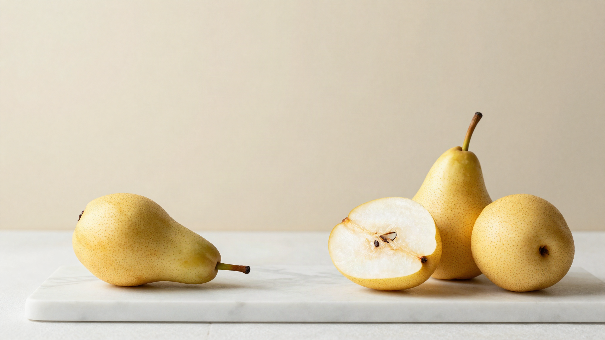 Two whole Williams pears and one halved on white marble showing pale grainy flesh