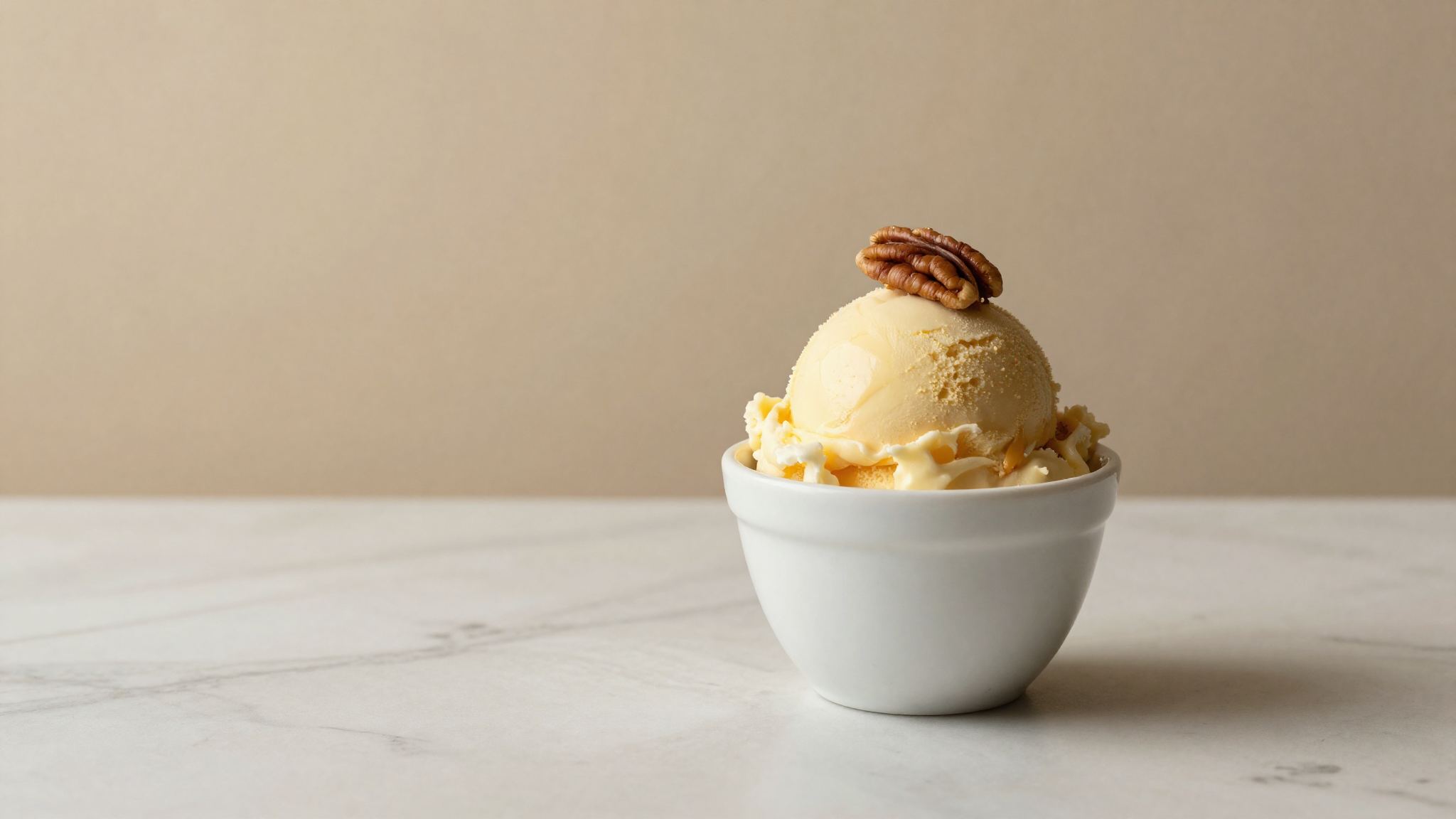 A scoop of butter-pecan gelato in a white ceramic cup garnished with a pecan half