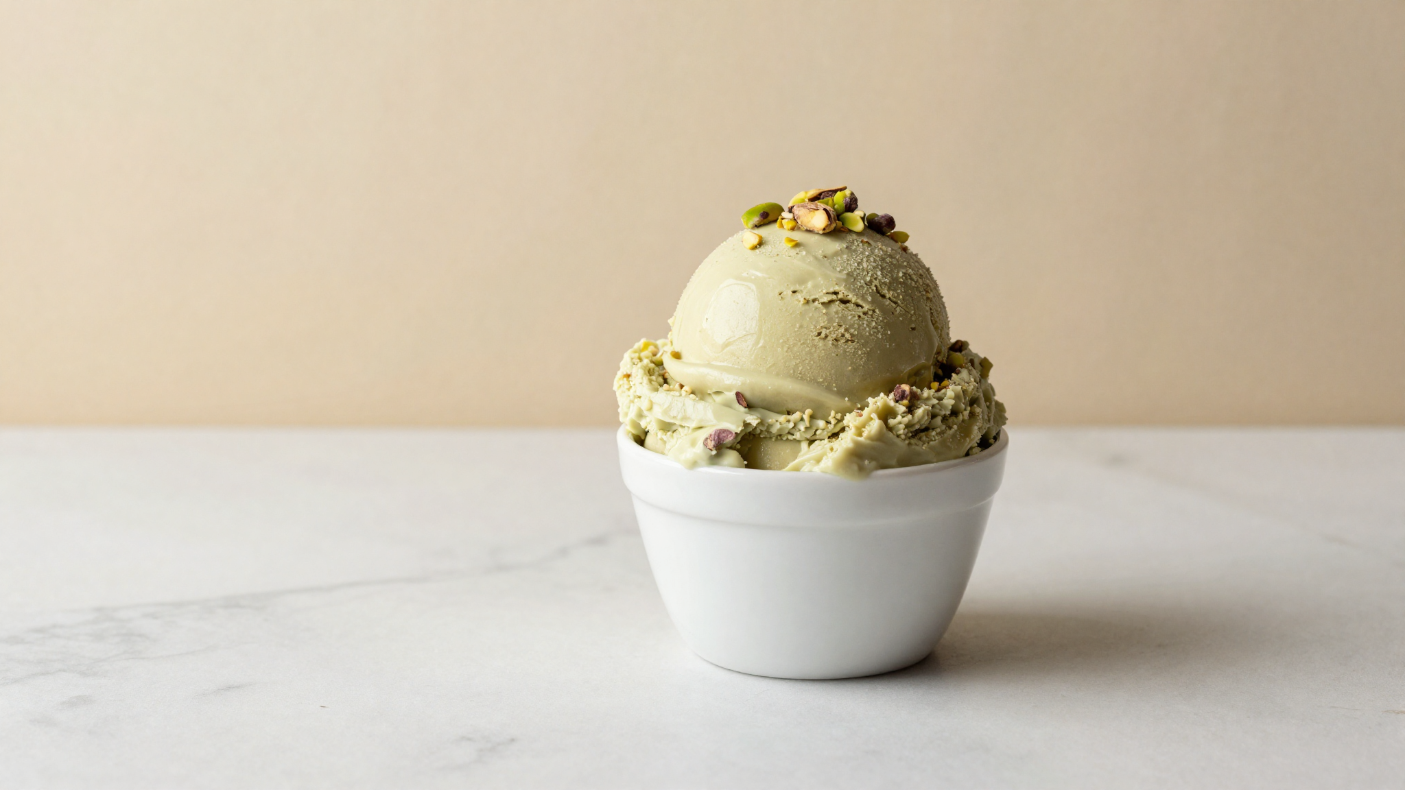 A scoop of muted-green vegan pistachio gelato in a ceramic cup topped with crushed pistachios