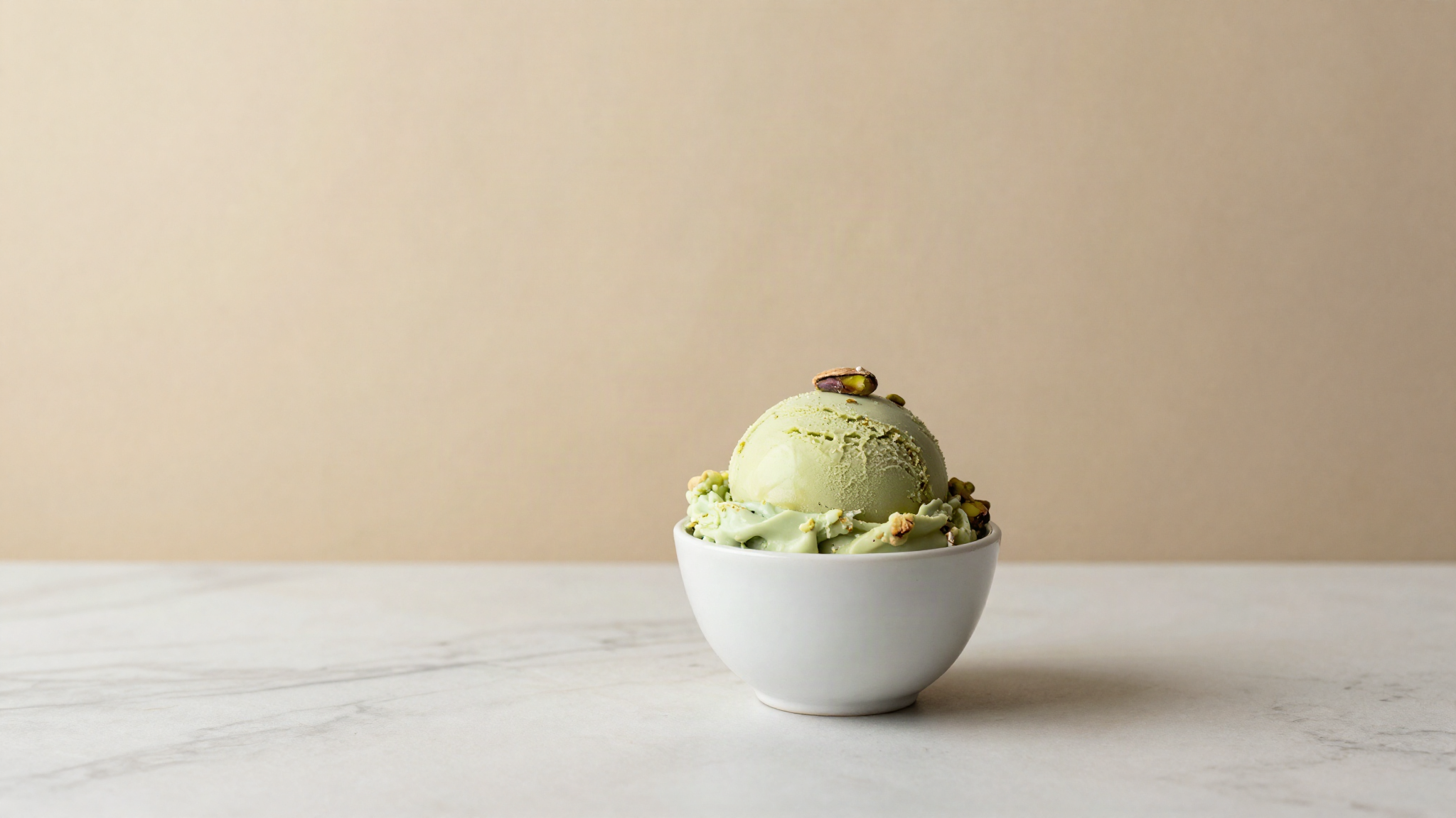 Scoop of pistachio gelato in a white ceramic cup on marble, showing natural green color