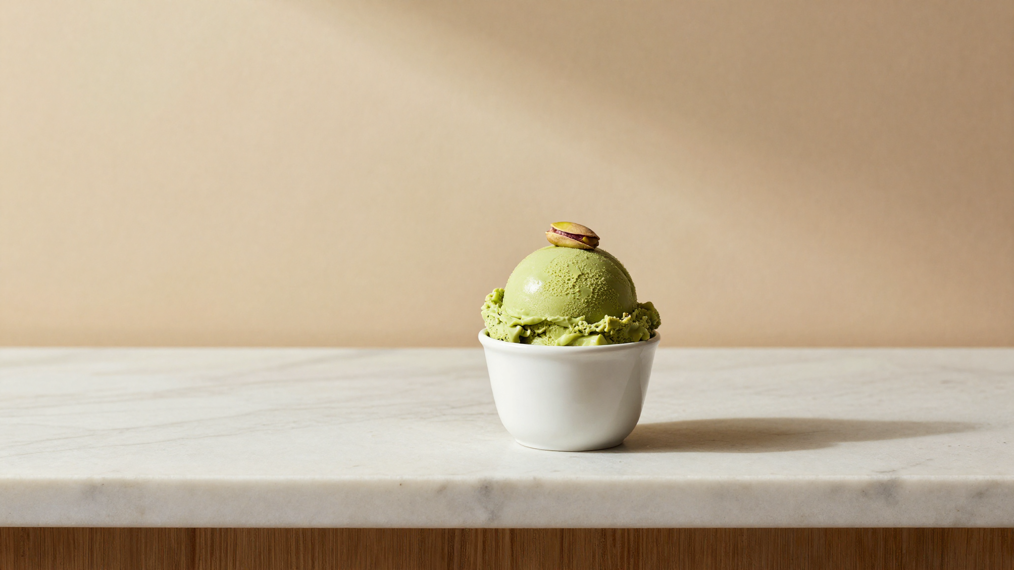 A scoop of vibrant green pistachio gelato in a white ceramic cup with a single pistachio garnish