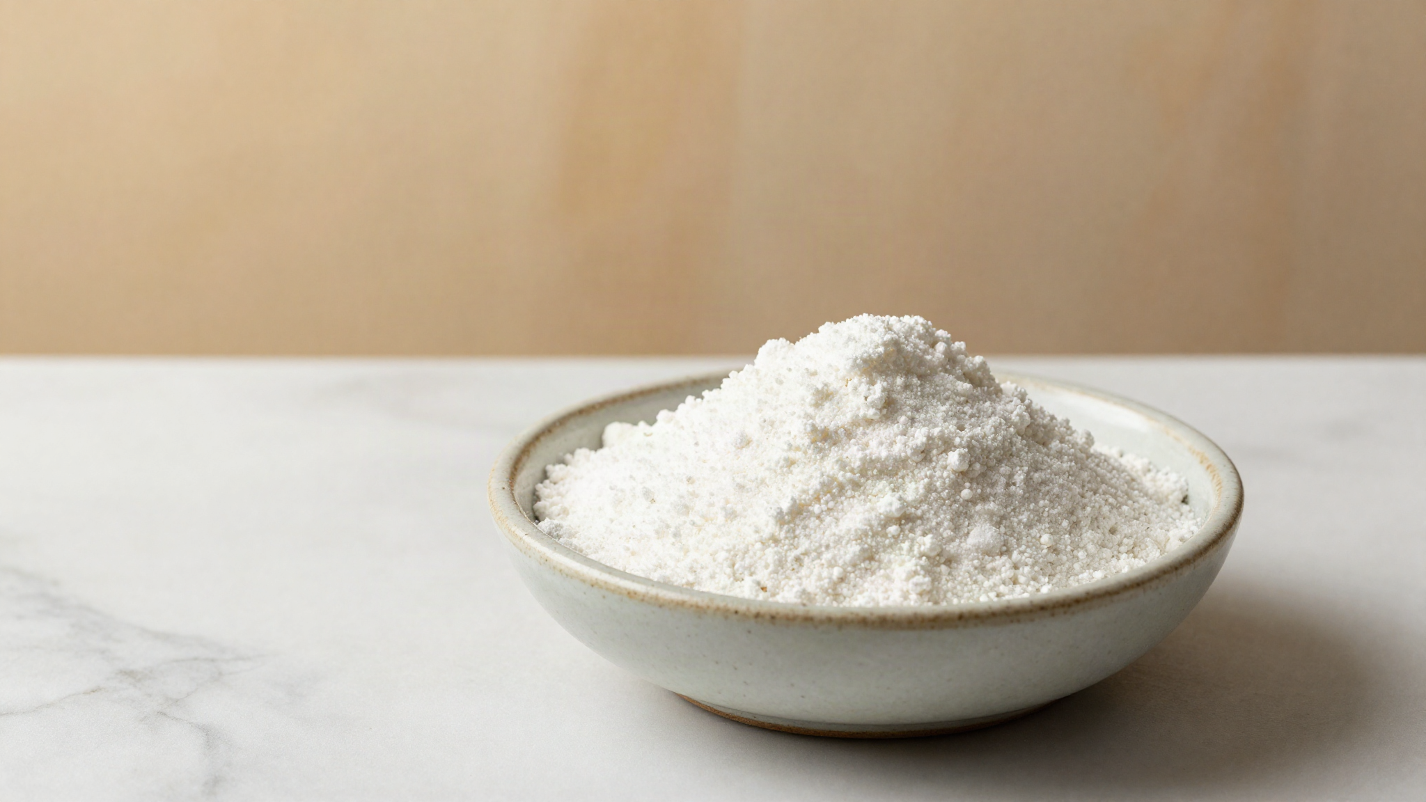 A small ceramic bowl of fine off-white polydextrose powder on a white marble surface