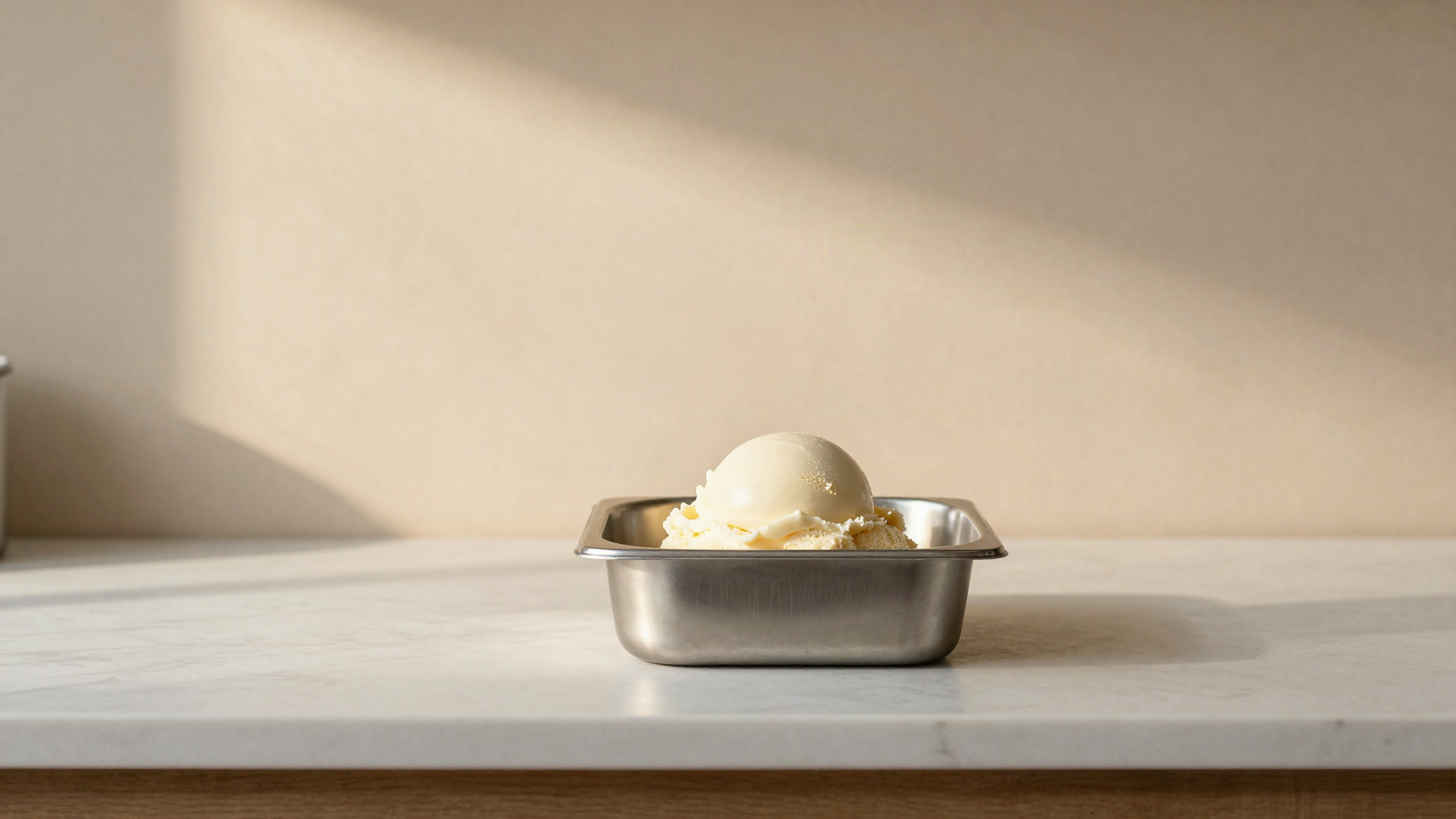 A small stainless steel container holding a scoop of pale gelato on a marble lab bench