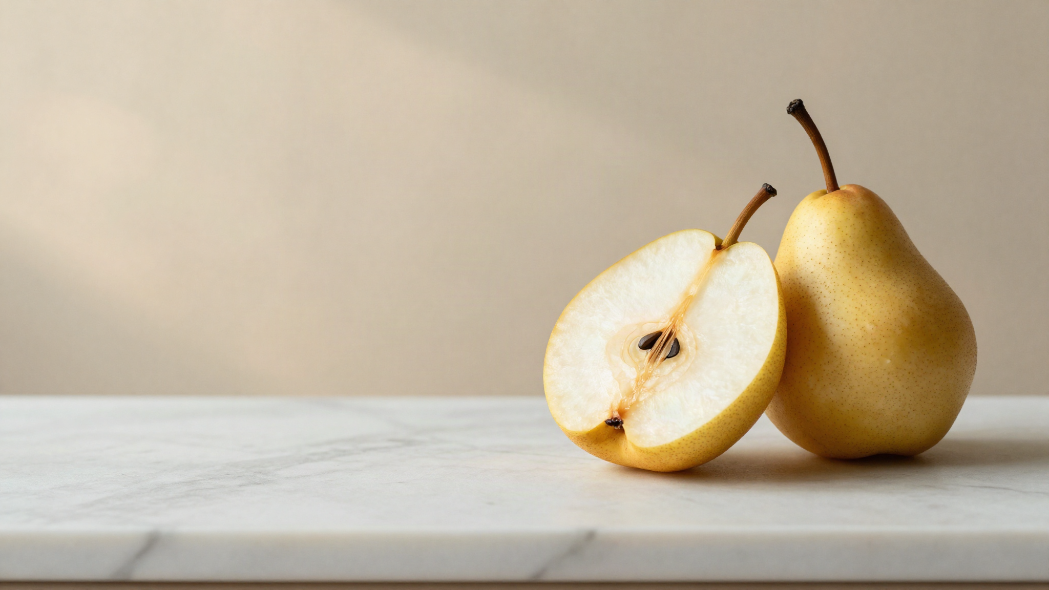 Freshly cut ripe pear and apple halves on white marble, one cut face still pale and another turned faintly amber brown