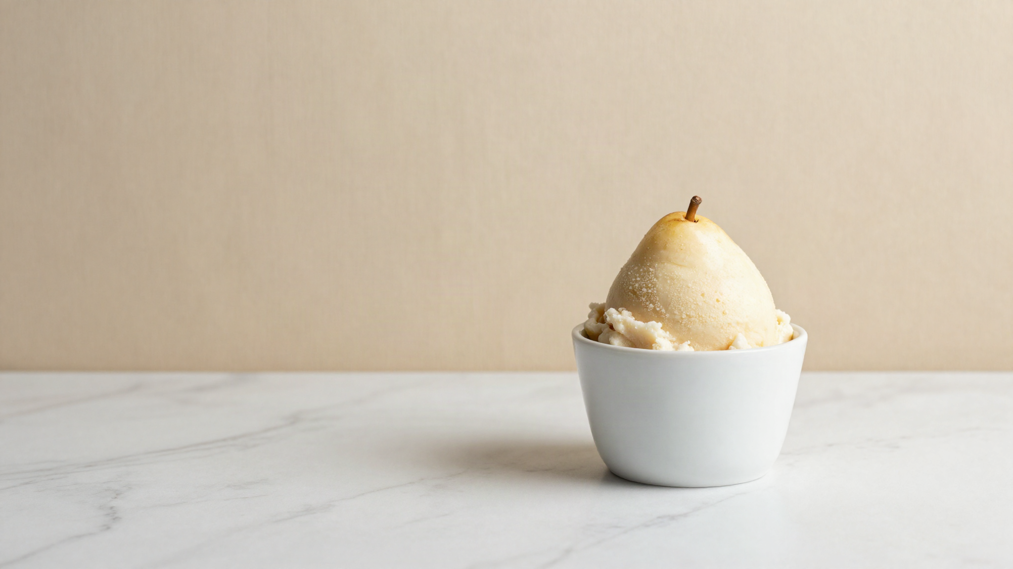 A scoop of pale ivory pear sorbet in a small white ceramic cup on white marble with bright clean fruit colour