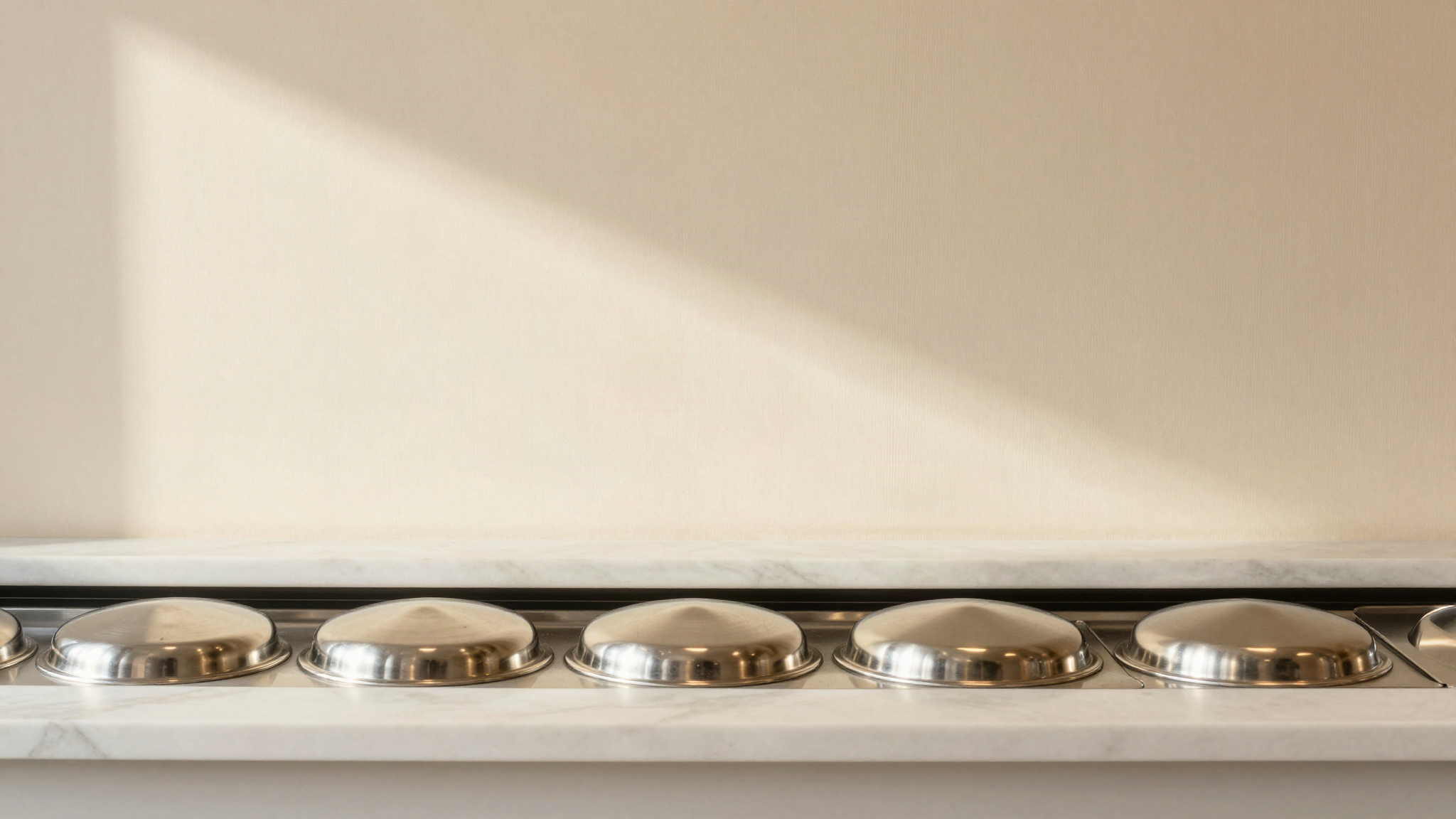 A row of round polished stainless steel pozzetti well lids set into a gelato counter