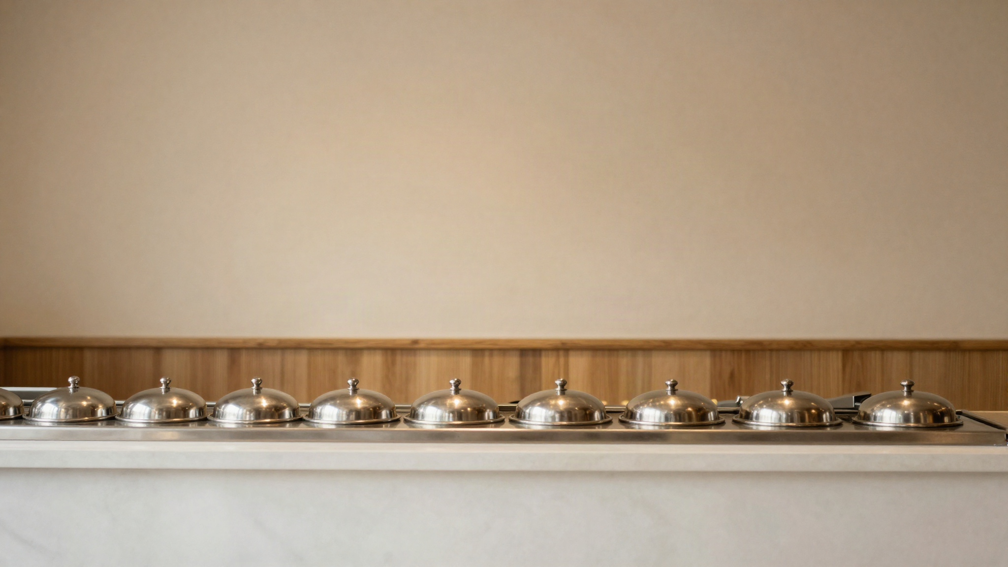 An italian gelateria service counter with a row of closed round stainless steel pozzetti lids