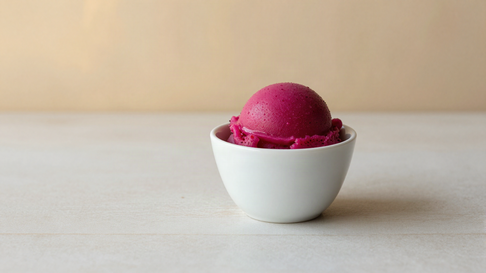 Vivid magenta prickly pear sorbetto quenelle in a white ceramic cup on marble