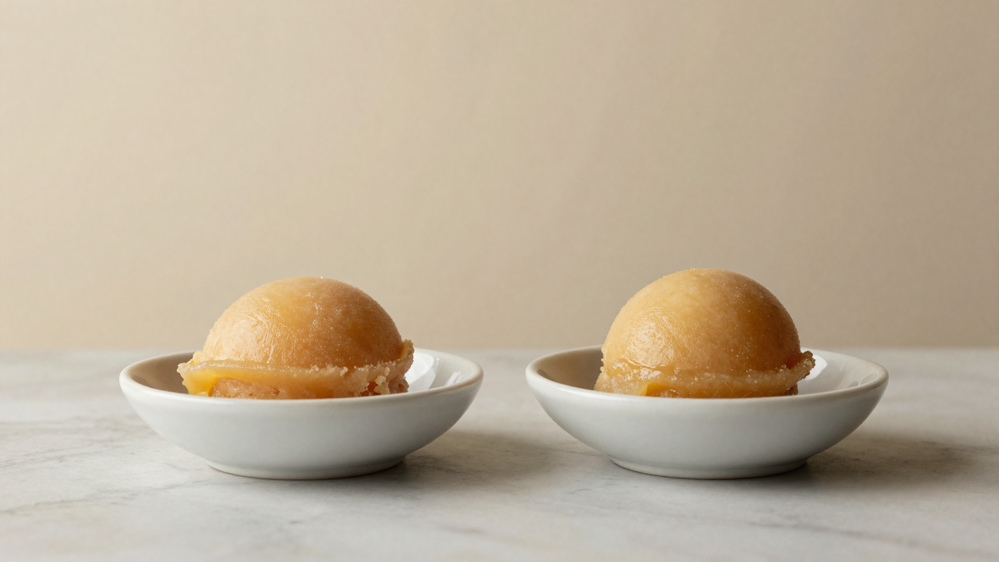 Two quenelles of fruit sorbet side by side, one glossy and smooth, one slightly coarse