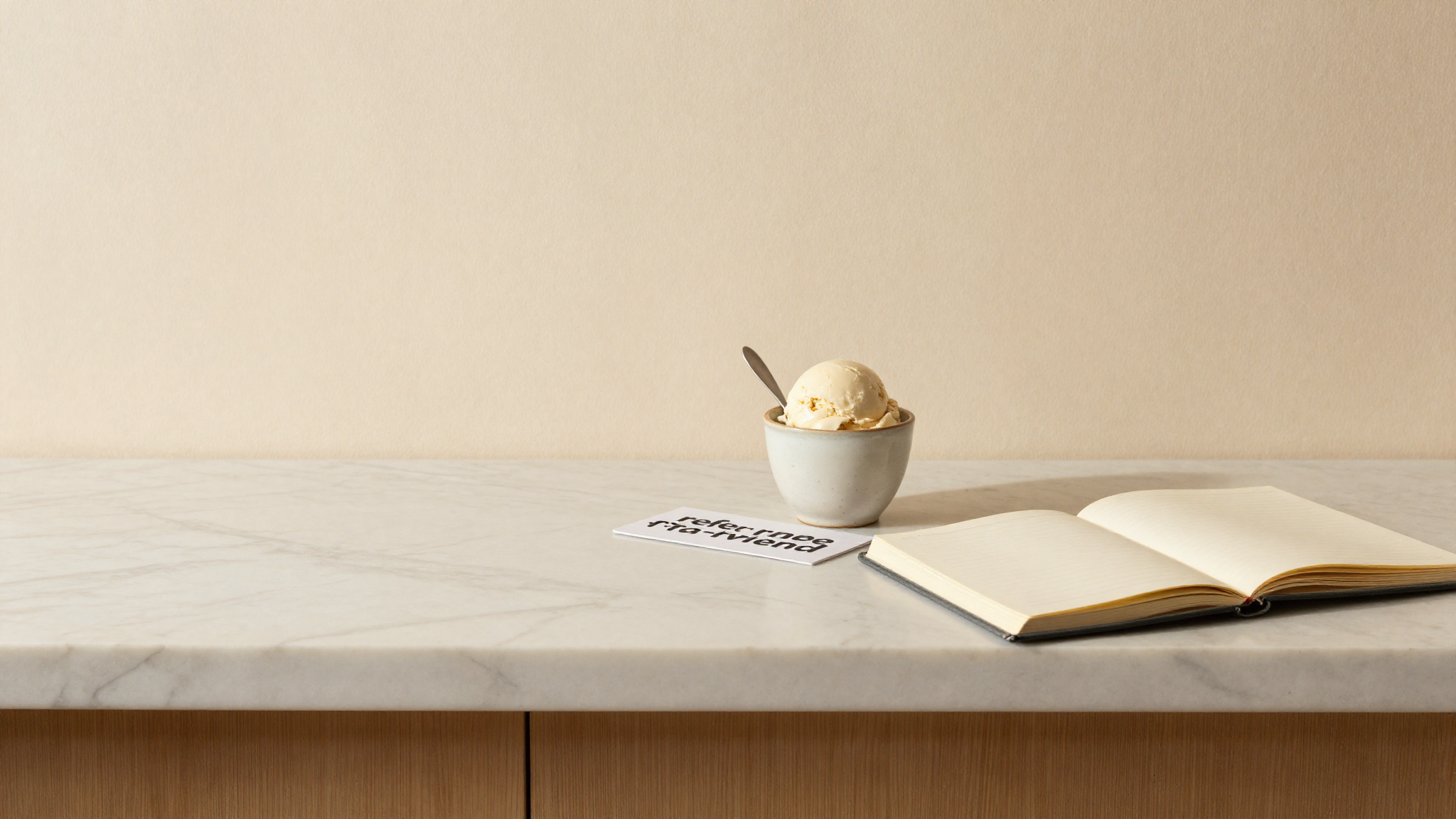 A marble counter with a cup of gelato, a refer-a-friend card and a notebook