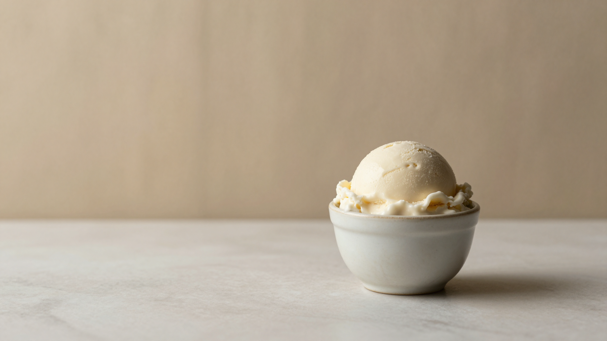A single elegant scoop of creamy pale gelato in a small ceramic cup on marble