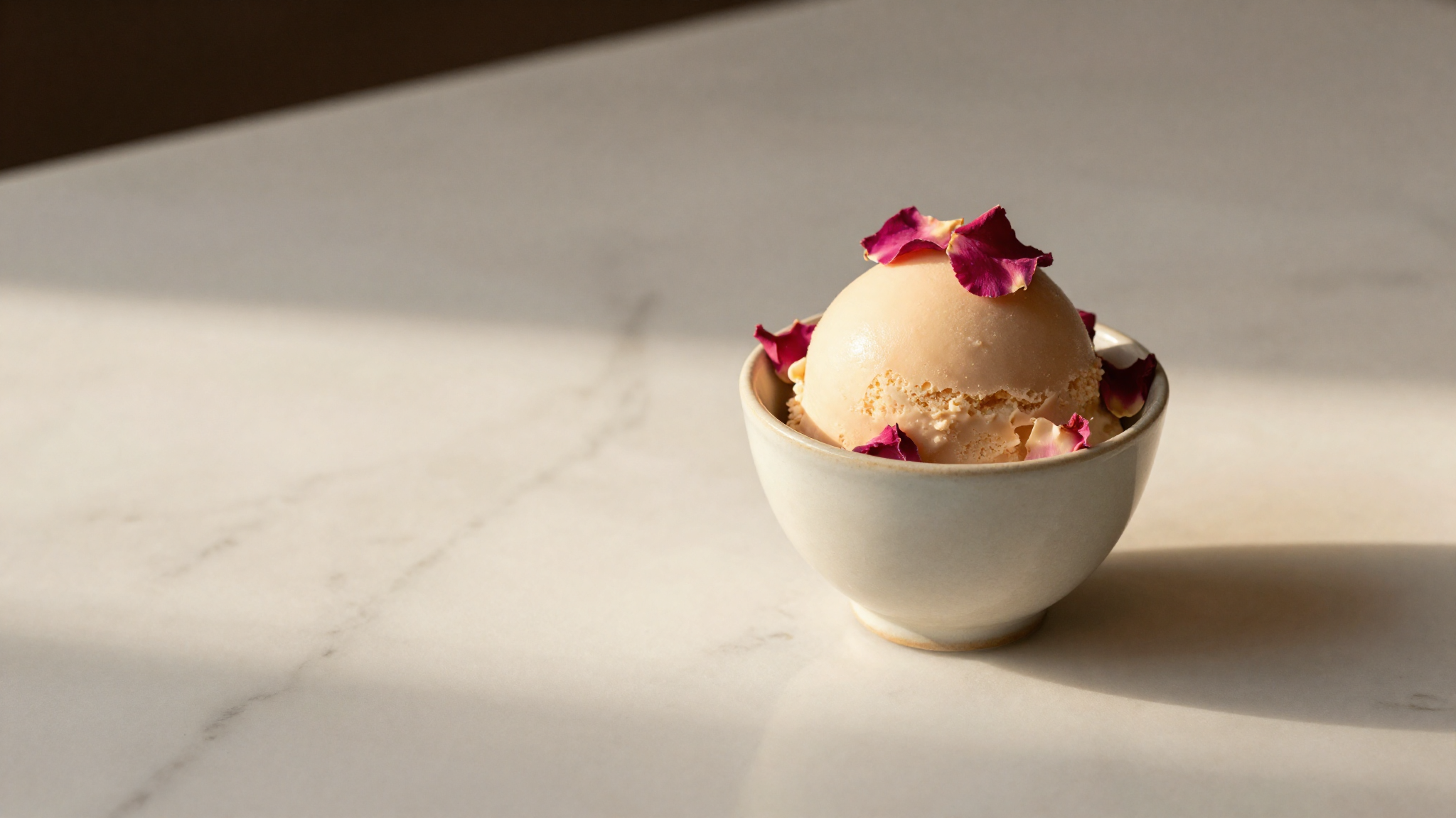 Rose water gelato in a small ceramic cup garnished with rose petals on marble