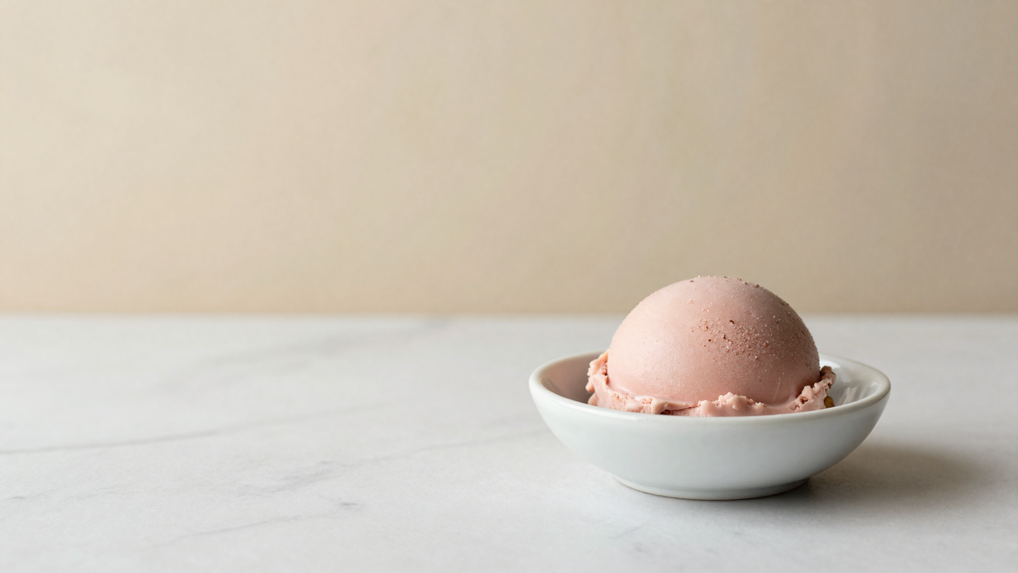 A scoop of pink ruby chocolate gelato in a small white dish on marble
