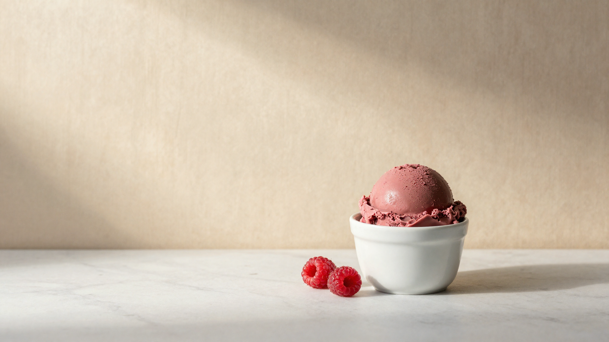 A scoop of pink ruby gelato in a white ceramic cup with a raspberry