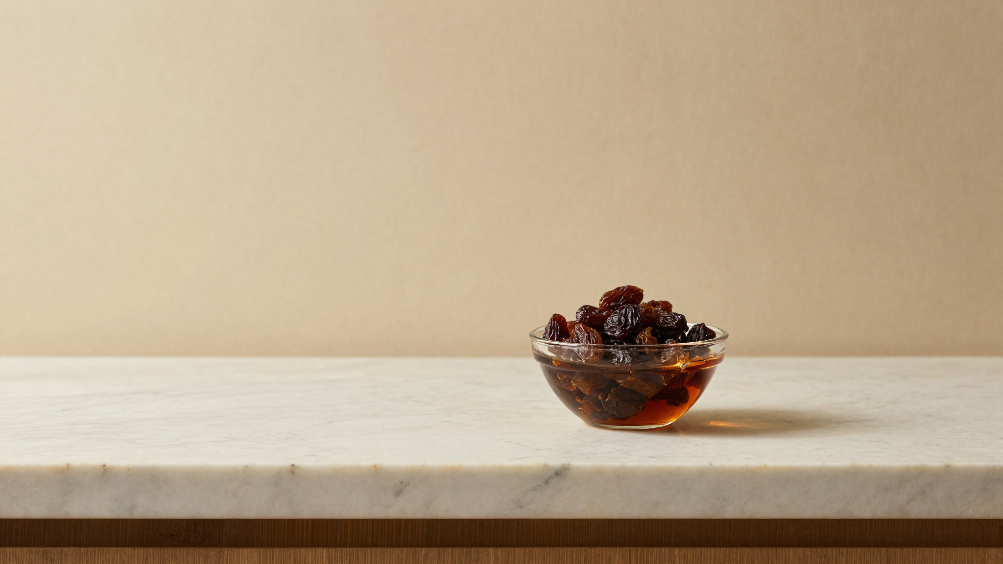Dark raisins soaking in amber rum in a glass bowl on marble