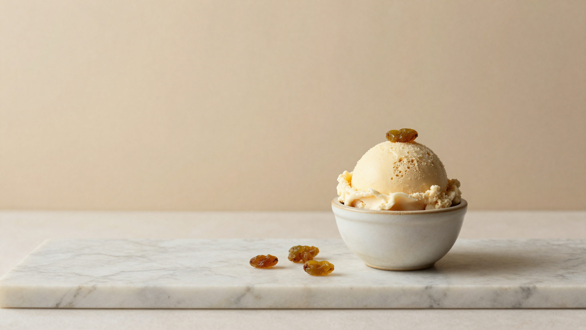 Refined scoop of rum raisin gelato in a small ceramic cup with scattered raisins