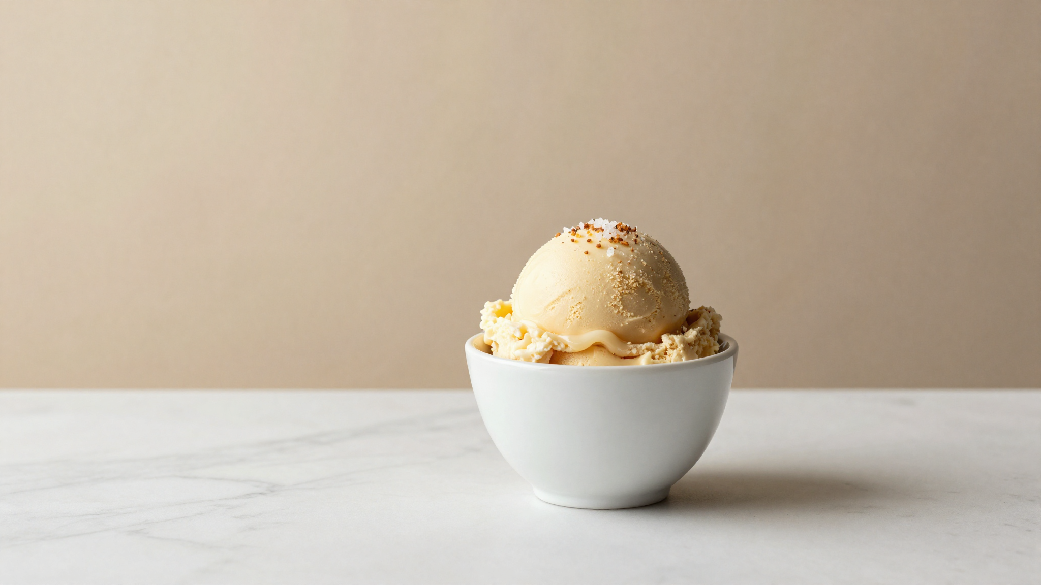 A finished scoop of salted caramel gelato topped with salt flakes in a white ceramic cup