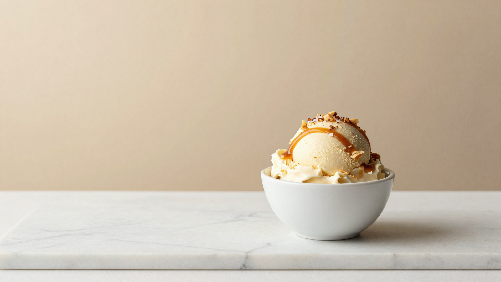 Salted caramel gelato in a ceramic cup finished with fleur de sel and caramel on white marble