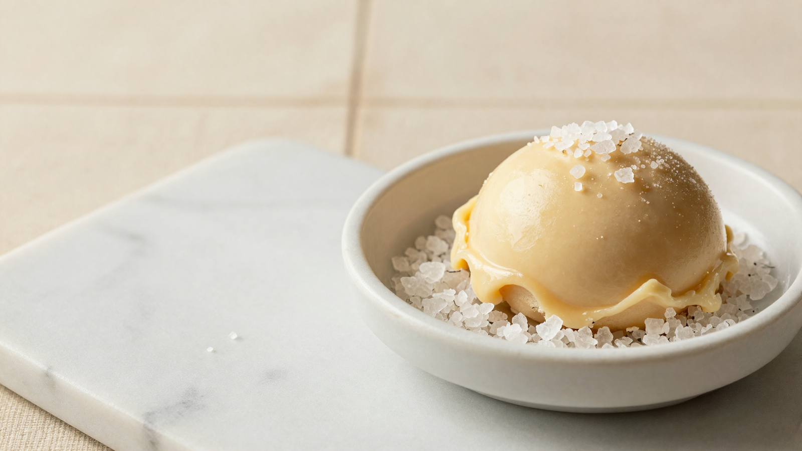Flaky fleur de sel crystals scattered over the surface of pale golden salted caramel gelato in a ceramic dish