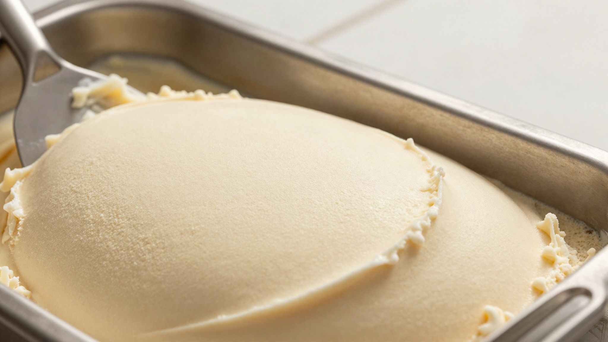 Close up of the cut surface of dense pale gelato in a stainless steel pan