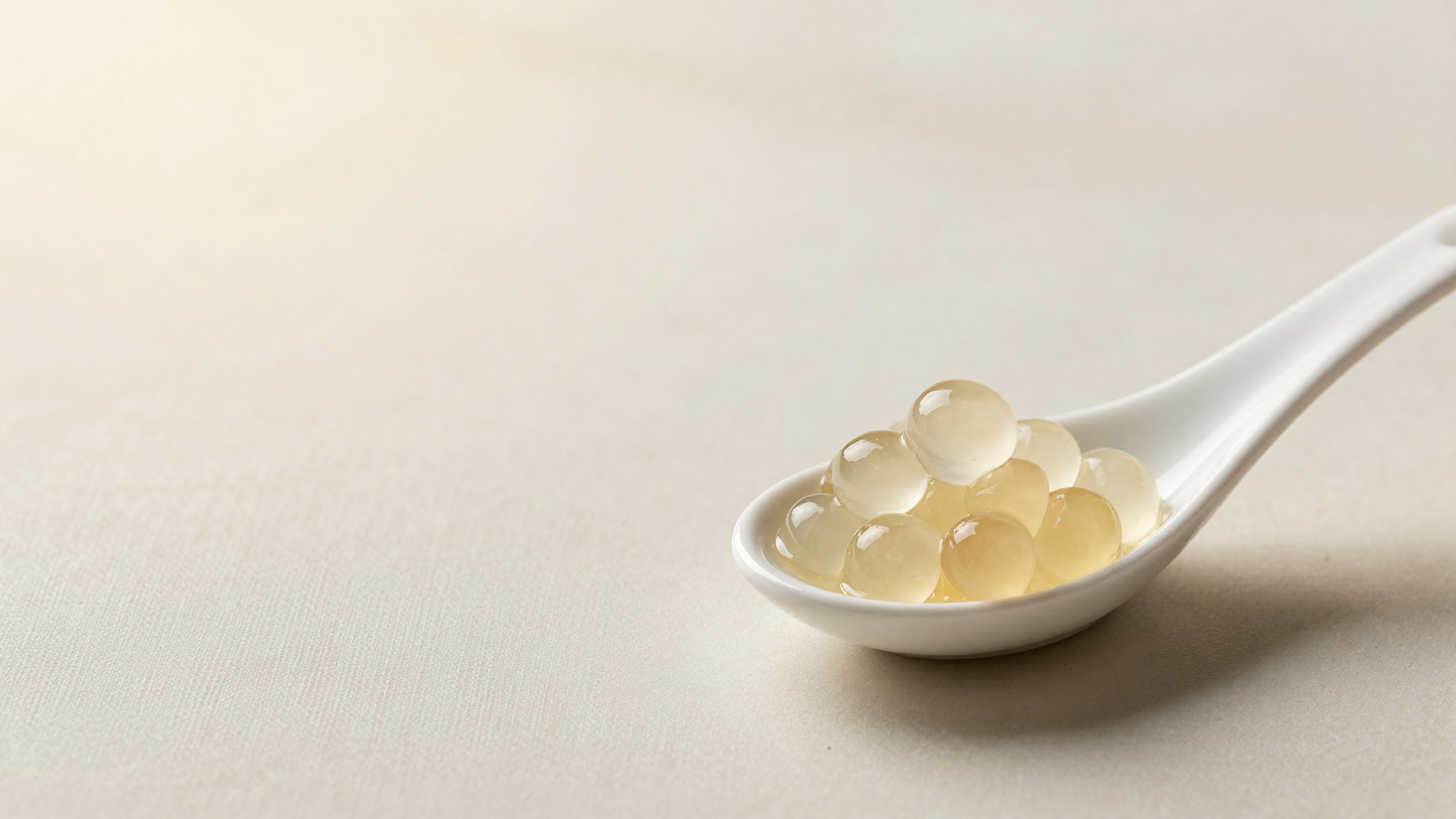 Small translucent liquid gelato spheres from spherification resting on a white ceramic spoon