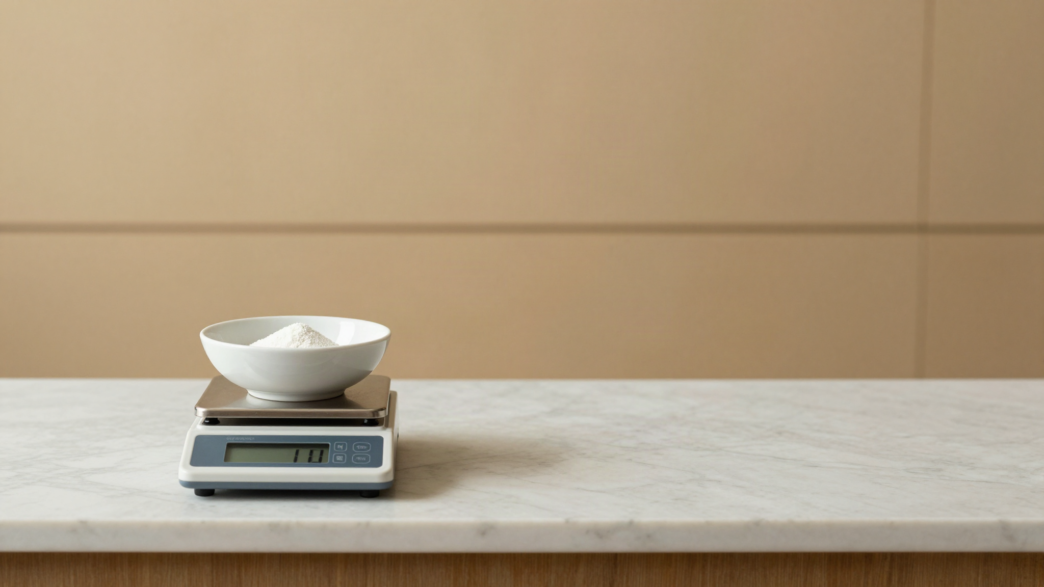 A digital gram scale holding a small ceramic bowl with a pinch of fine white powder on a marble counter
