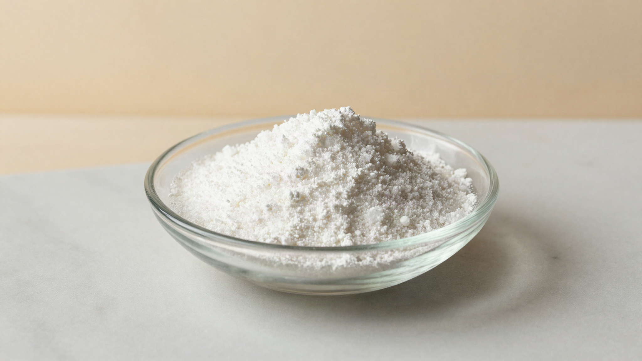 Fine white sorbitol powder in a small clear glass dish on a white marble surface