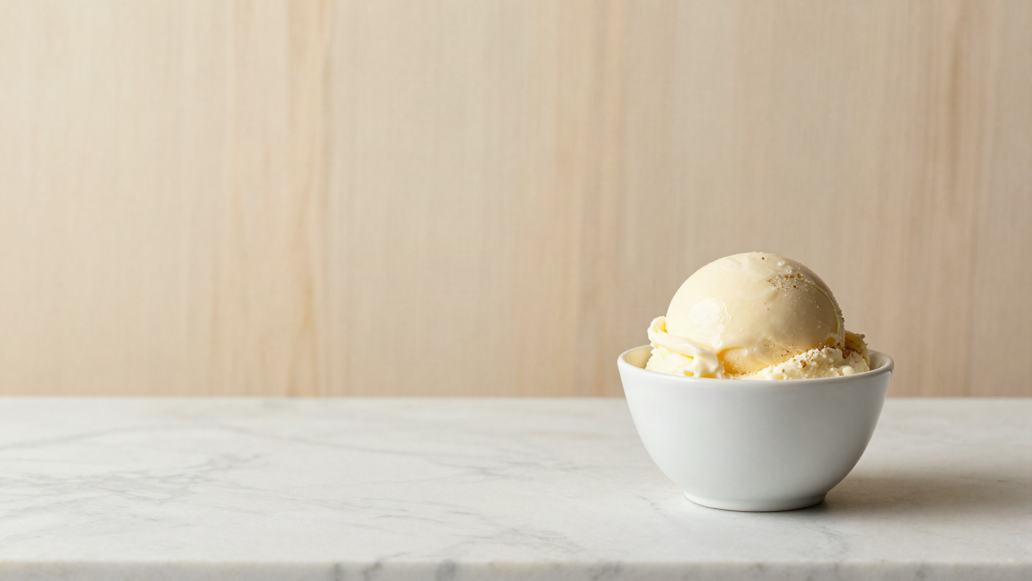 A smooth soft scoop of pale vanilla gelato in a small white ceramic cup on marble
