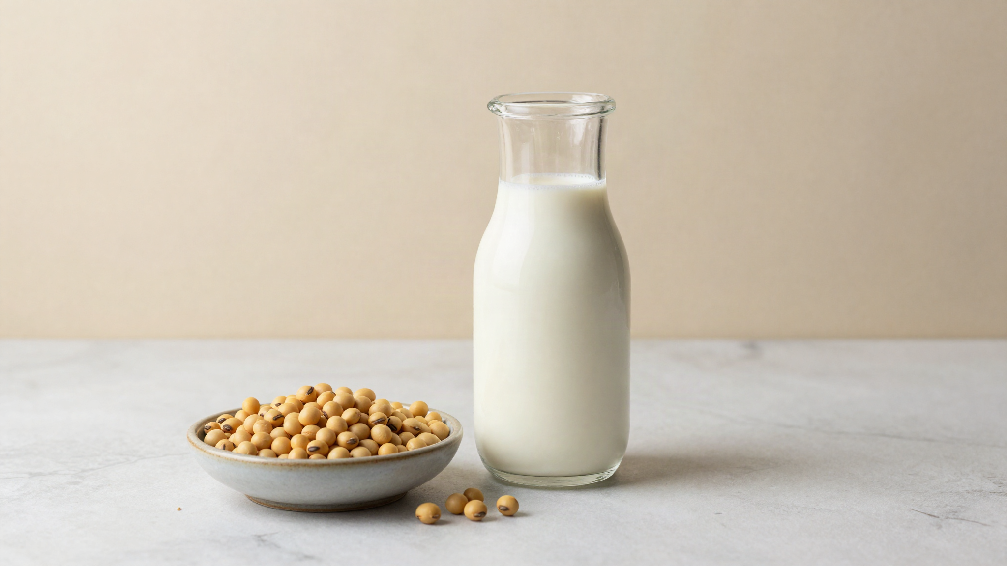 Glass carafe of soy milk beside whole dried soybeans on a marble surface