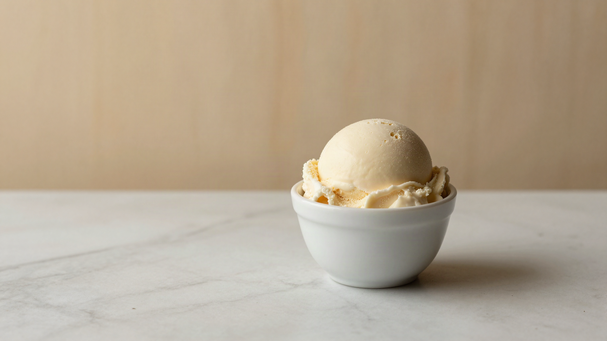 A smooth scoop of pale vegan soy gelato in a white ceramic cup on marble