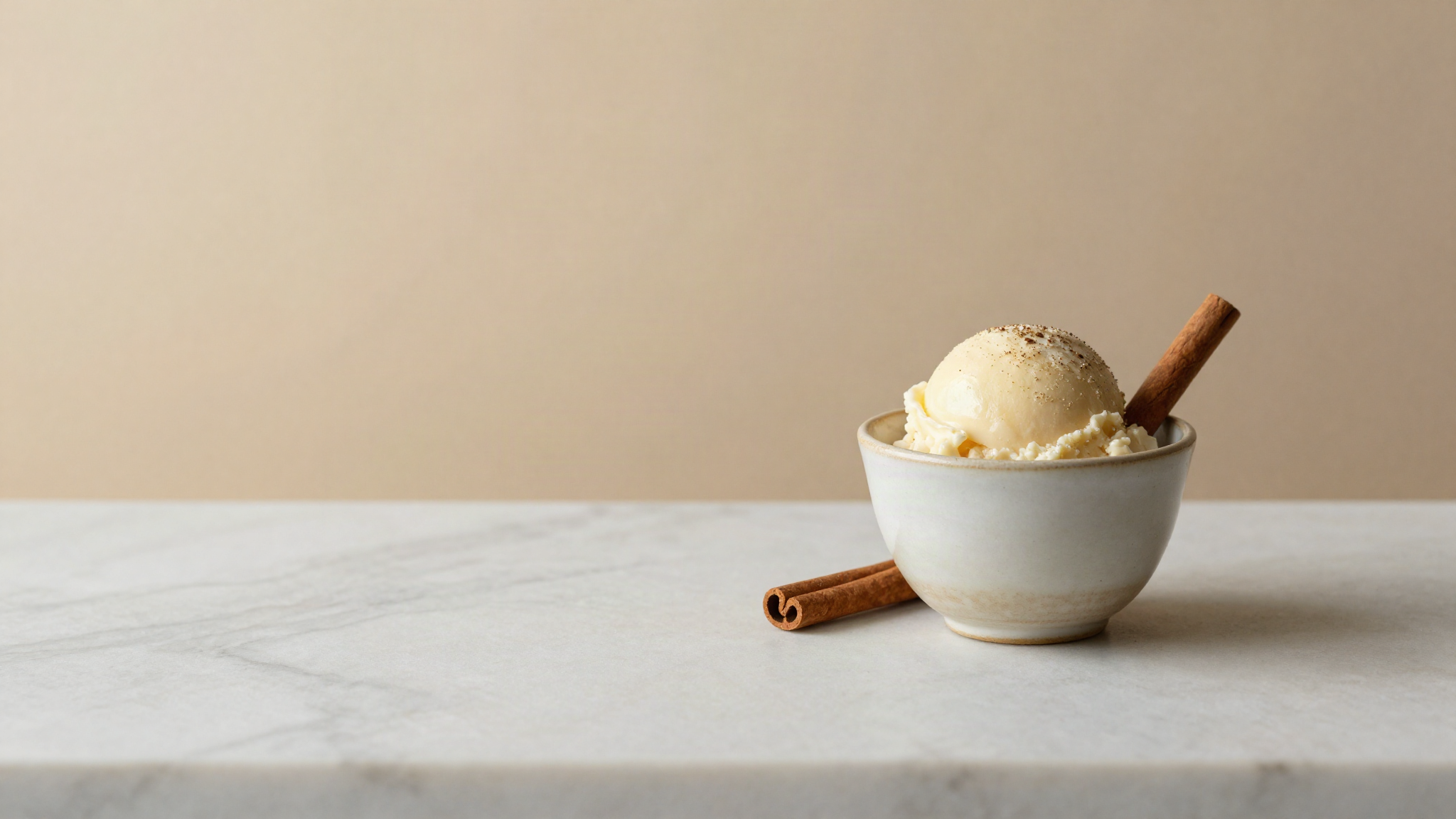 Small ceramic cup of pale spiced gelato with a single cinnamon stick beside it on marble