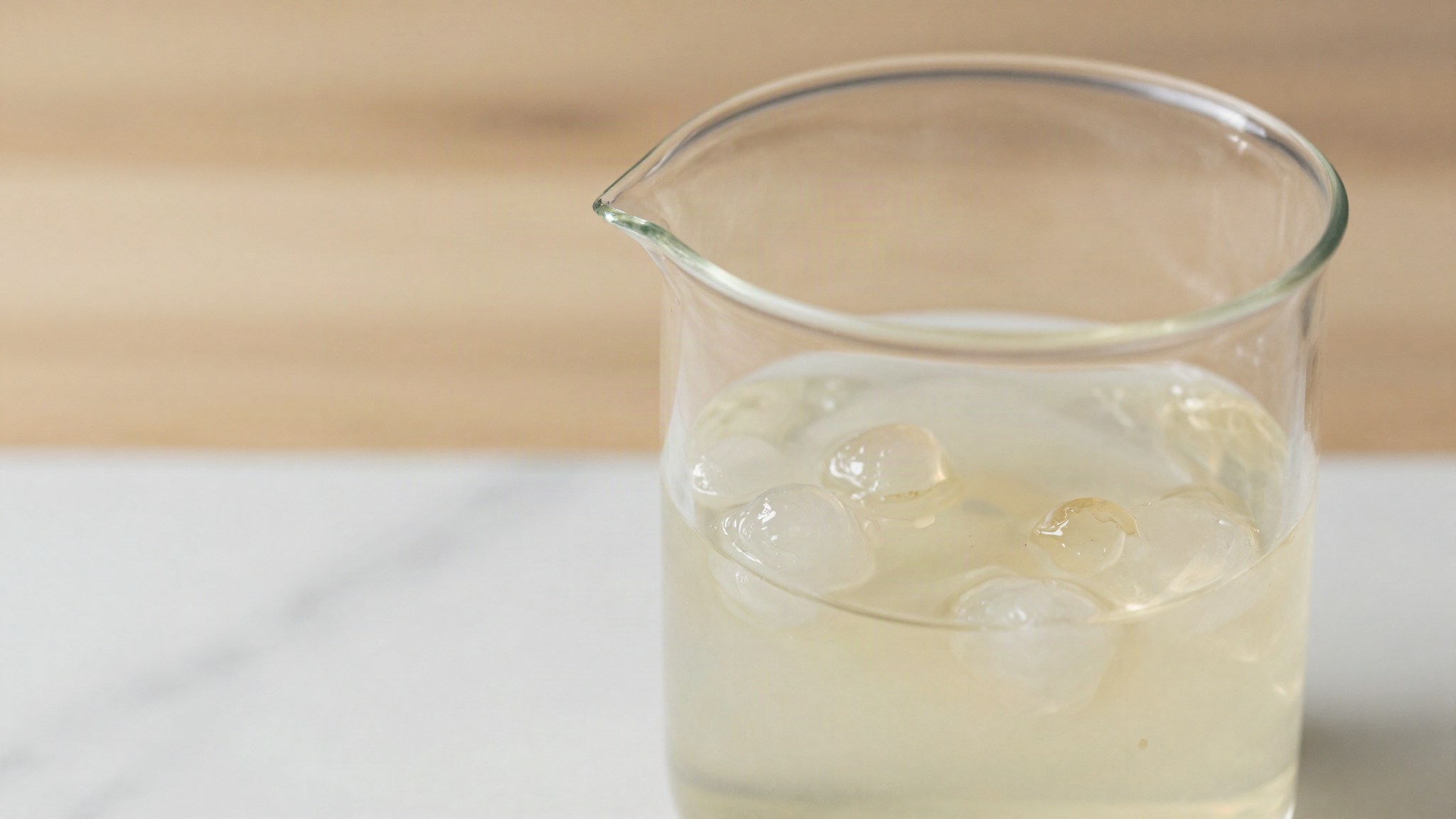 Small translucent gel lumps floating in a pale milky liquid inside a clear glass beaker on marble