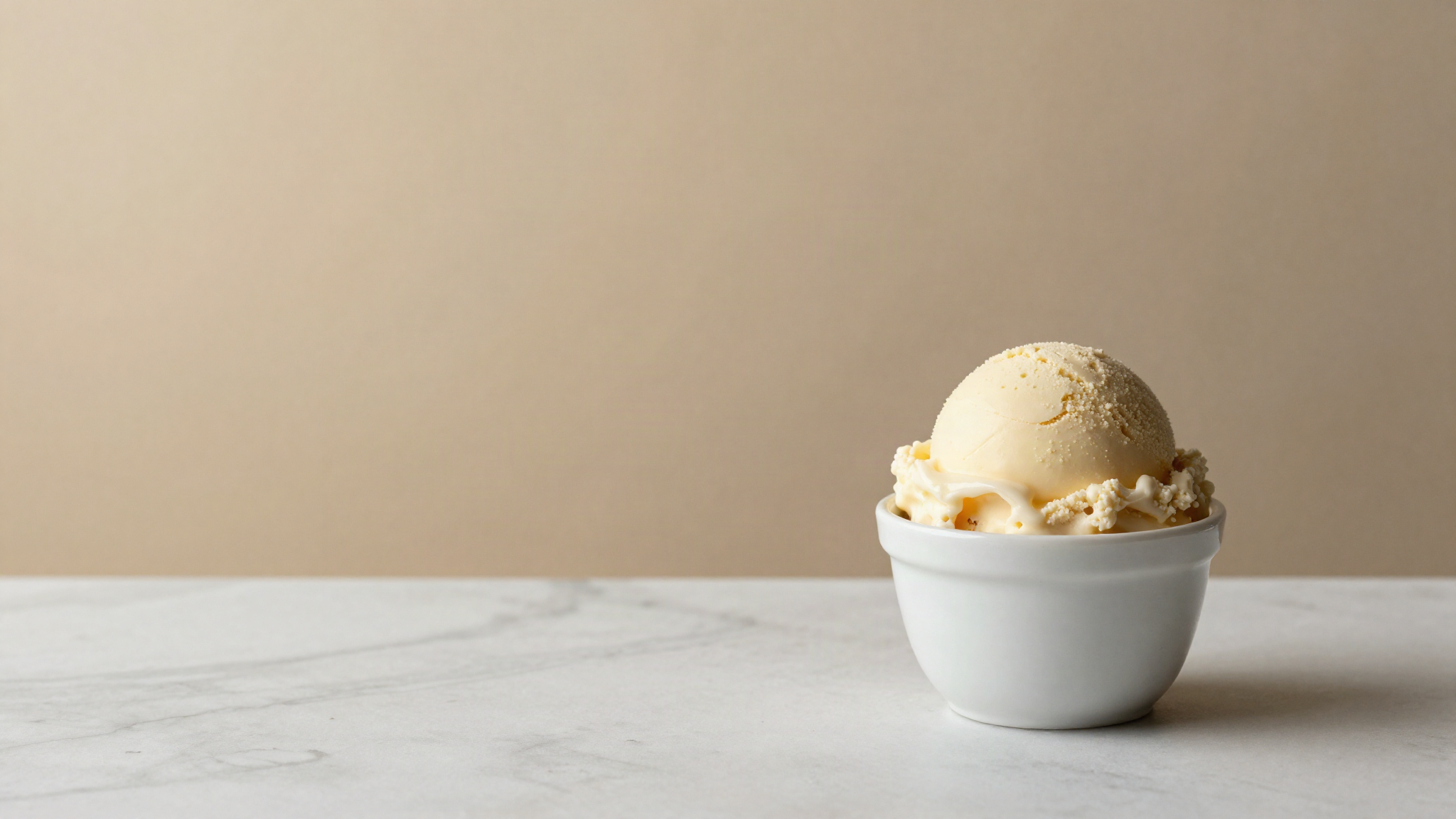 Dense scoop of italian gelato in a small white ceramic cup on a marble counter