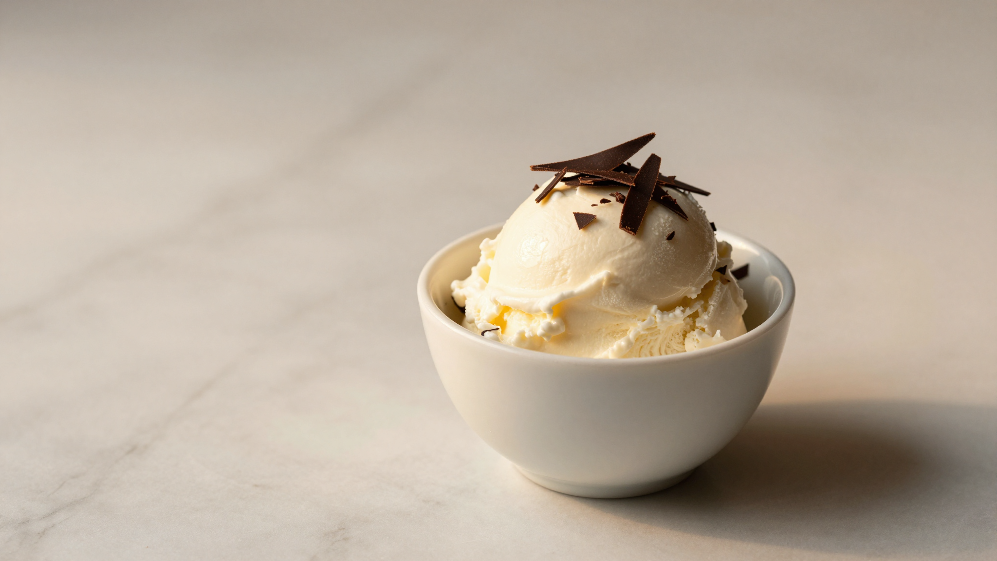 Finished stracciatella fior di latte gelato in a white ceramic cup with dark chocolate shards on marble