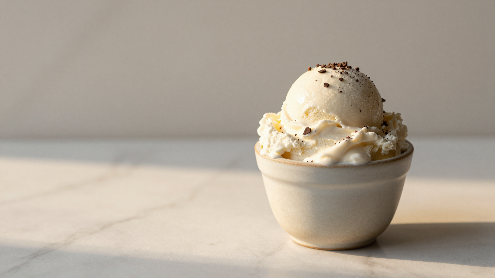 Single scoop of stracciatella gelato showing fine dark chocolate shards in white cream in a ceramic cup