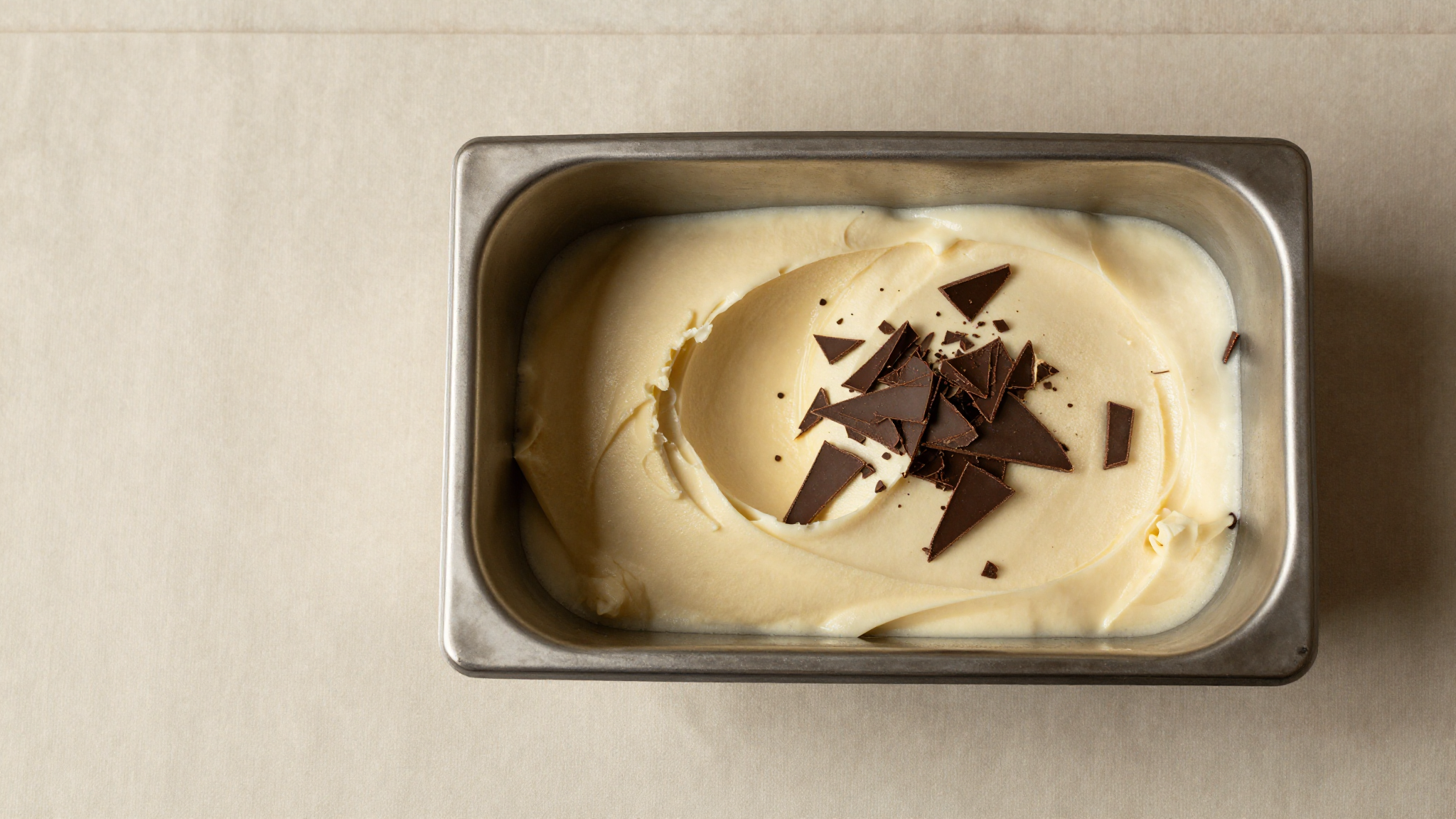 Thin shards of dark chocolate dispersed through cream colored gelato top down still life on marble