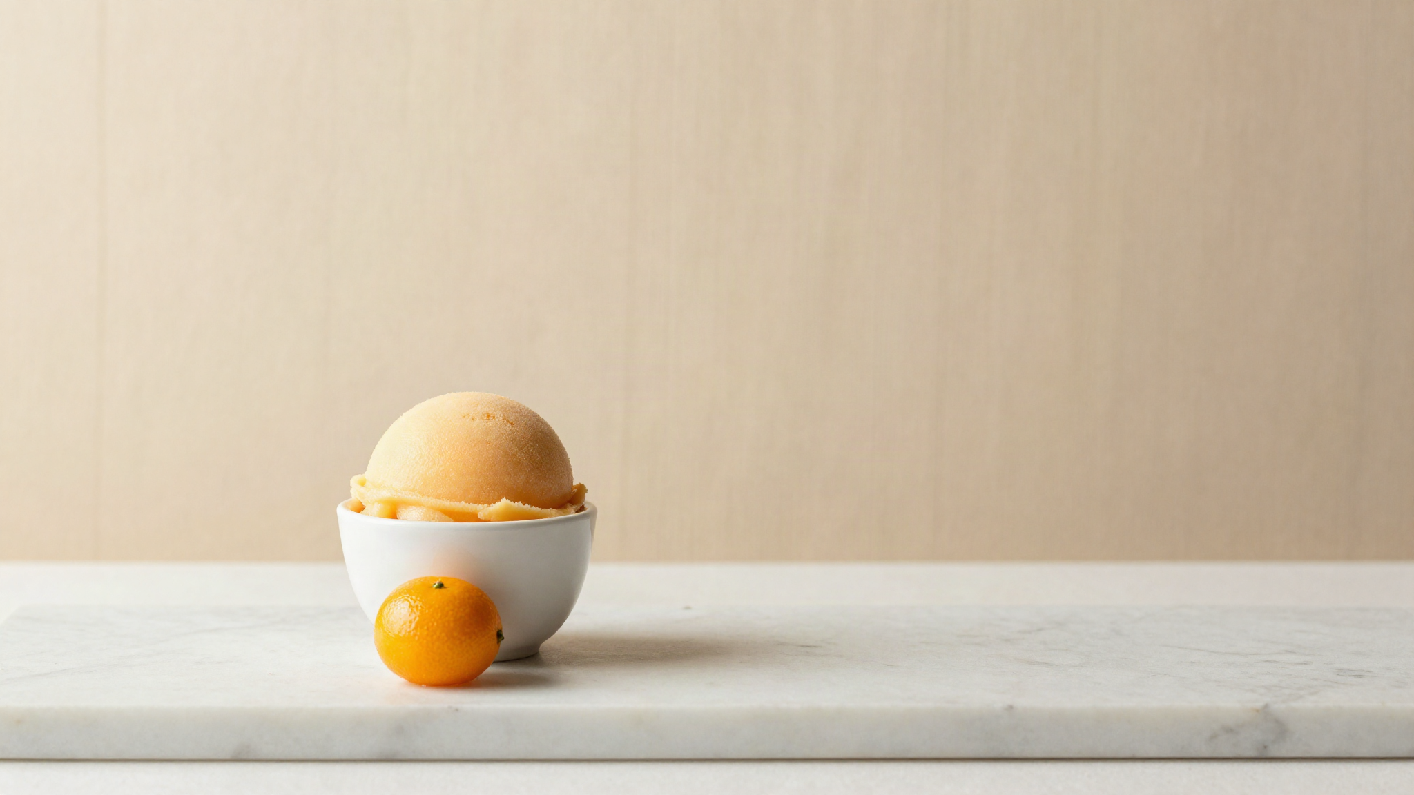A quenelle of pale orange citrus sorbet in a small white ceramic cup with a single supreme beside it
