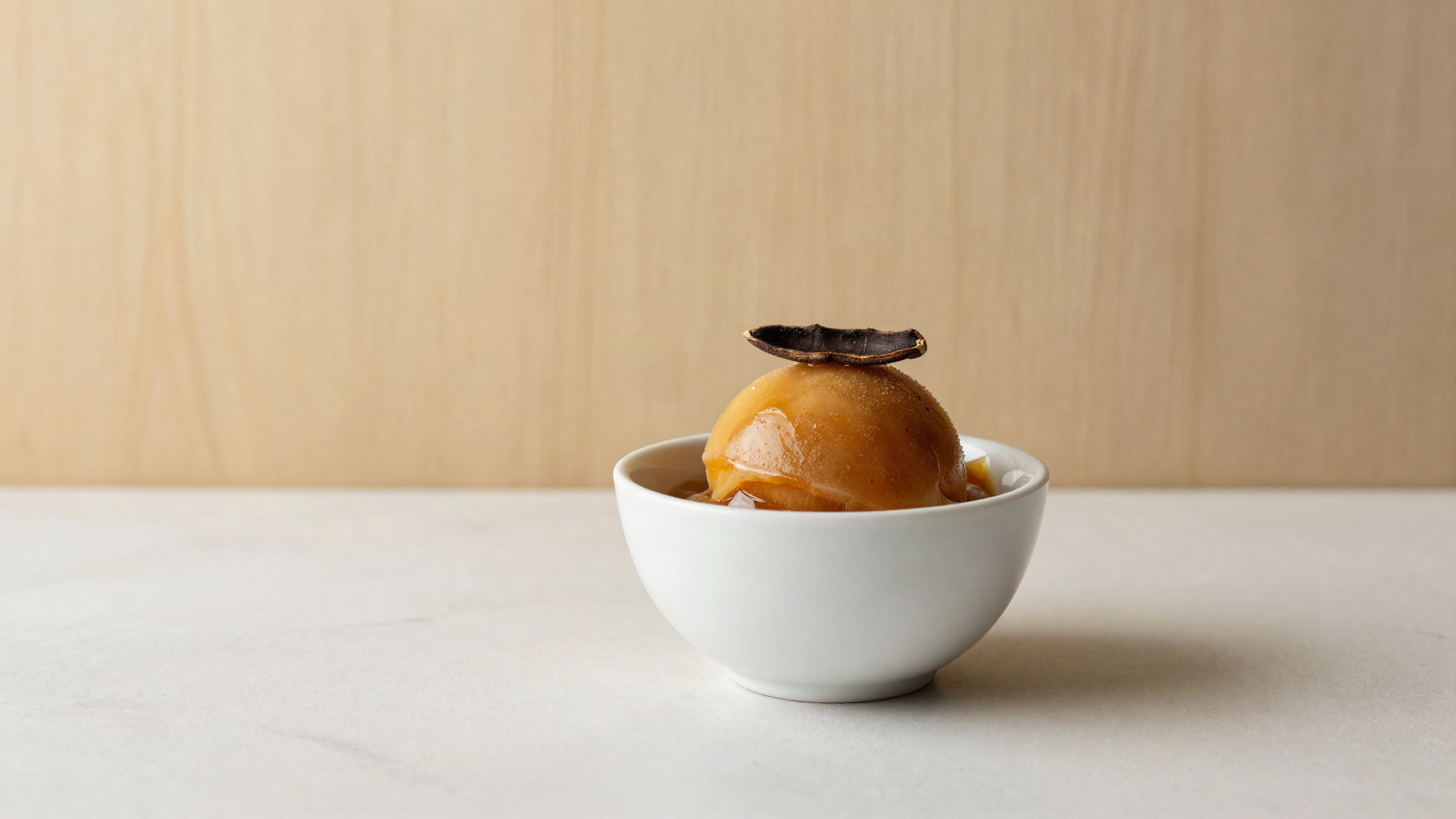 Dark amber tamarind sorbetto served in a small white ceramic cup on marble