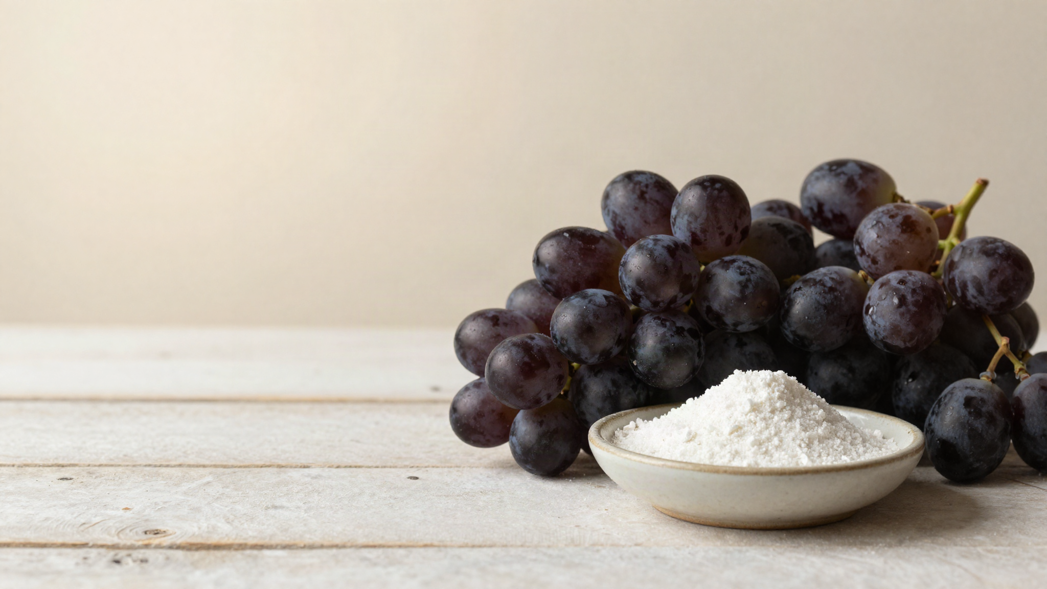 A bunch of dark wine grapes beside a small ceramic dish of fine white crystalline acid on aged wood