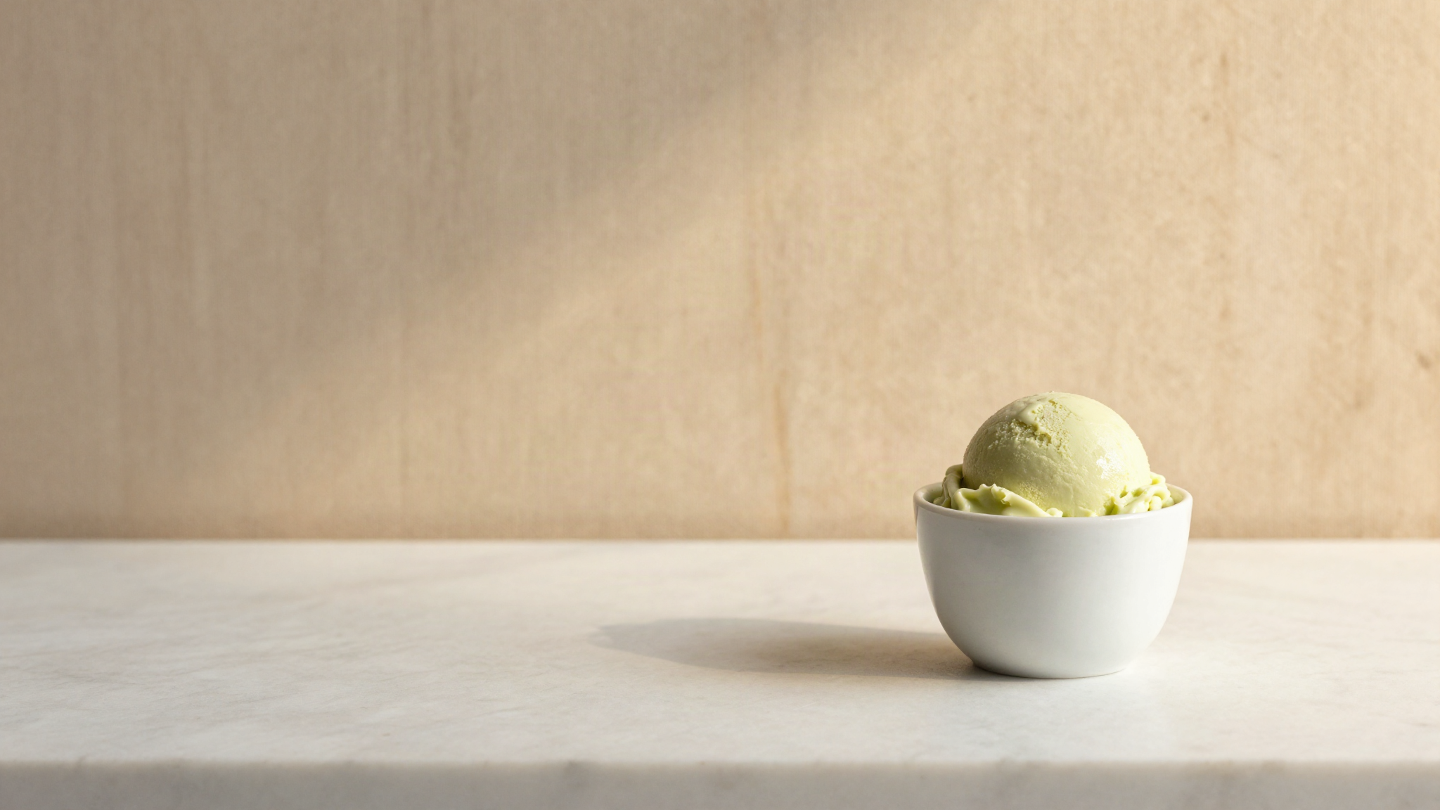 A single scoop of pale green apple sorbetto in a small white ceramic cup on marble