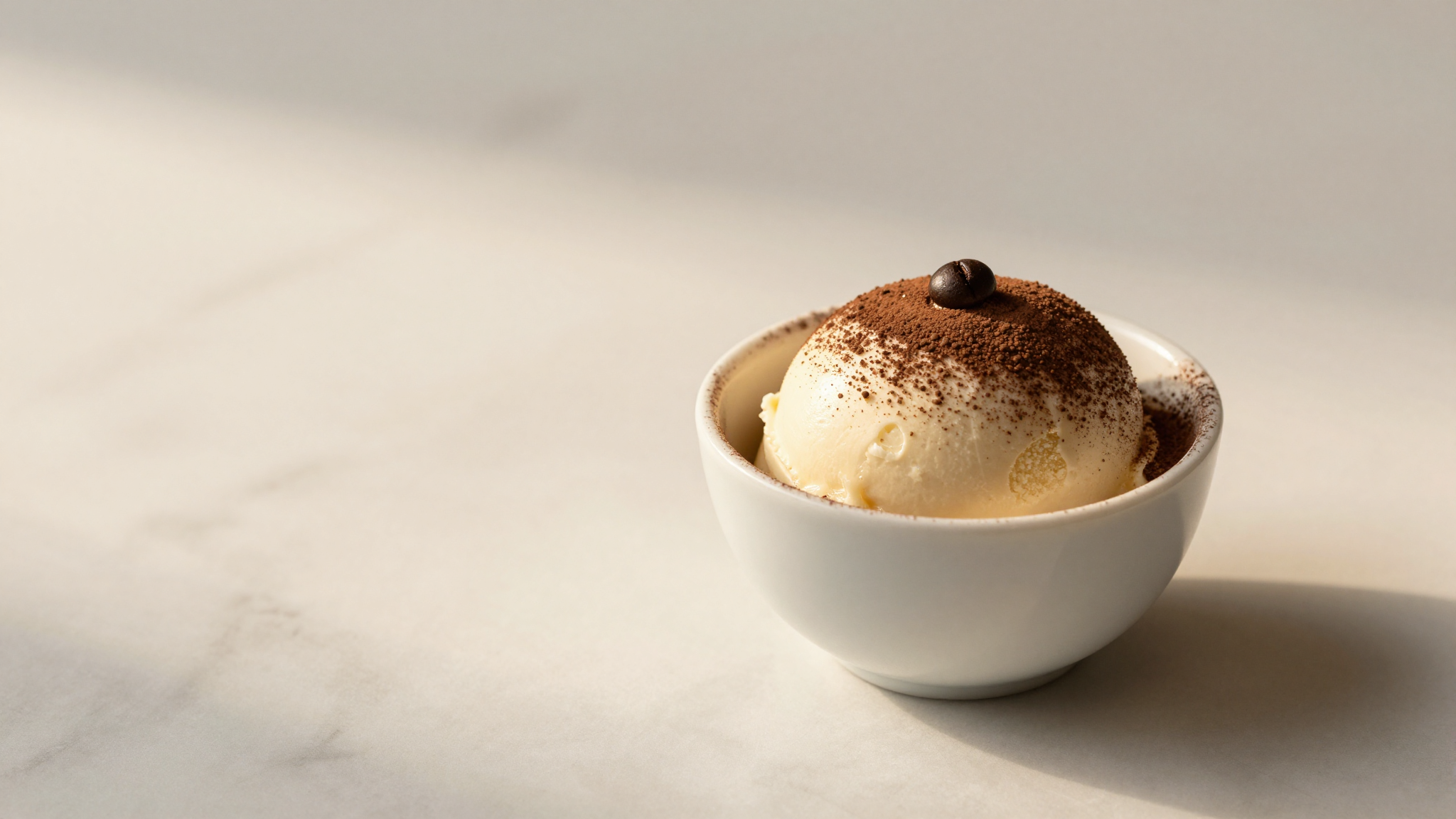 Scoop of tiramisu gelato in a white ceramic cup on marble with cocoa dusting
